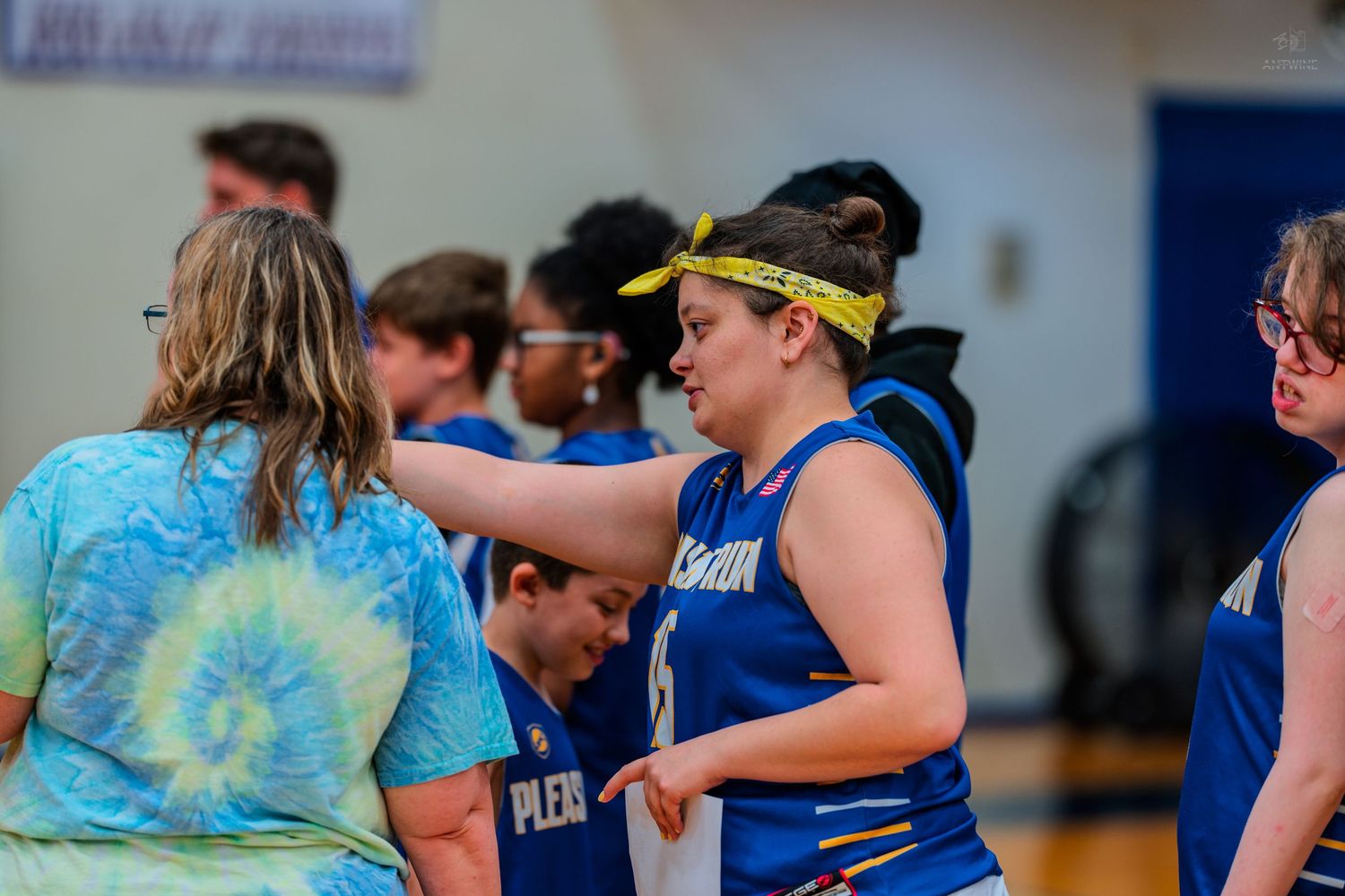 Young basketball player in blue uniform with yellow headband receives coaching during an indoor game.