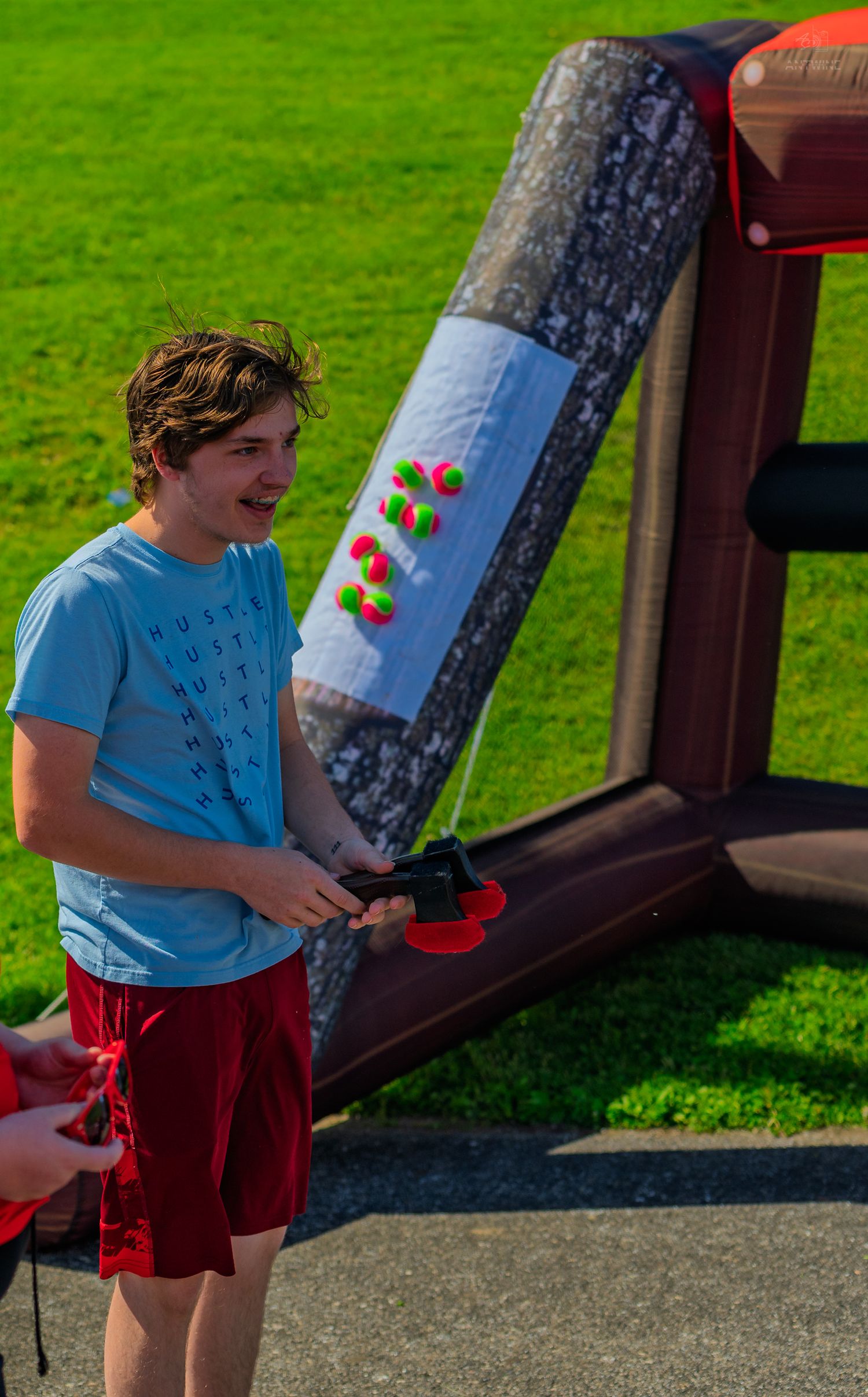 Teen boy in blue shirt playing inflatable carnival game outdoors on sunny day at festival event.