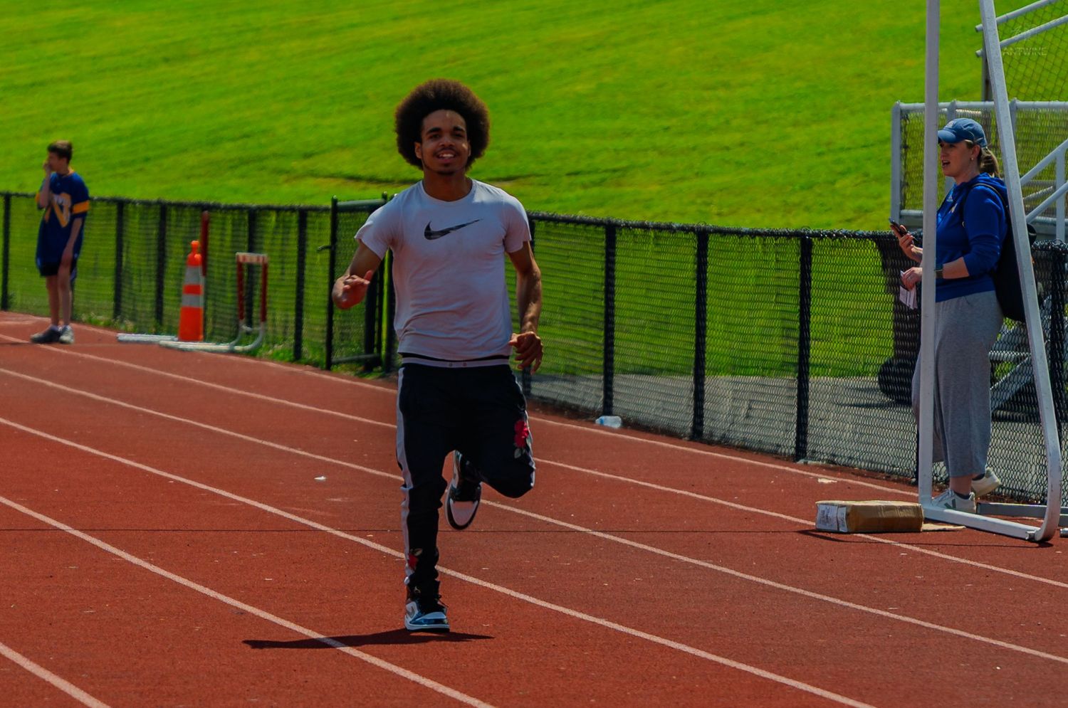 Young athlete sprinting on a red track during an outdoor track and field meet, wearing a Nike shirt.