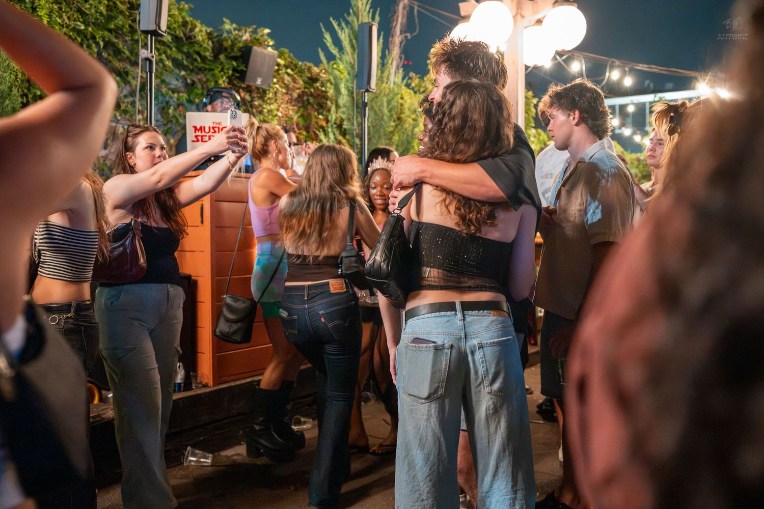Group of young friends hugging and taking selfies at an outdoor nighttime social gathering.