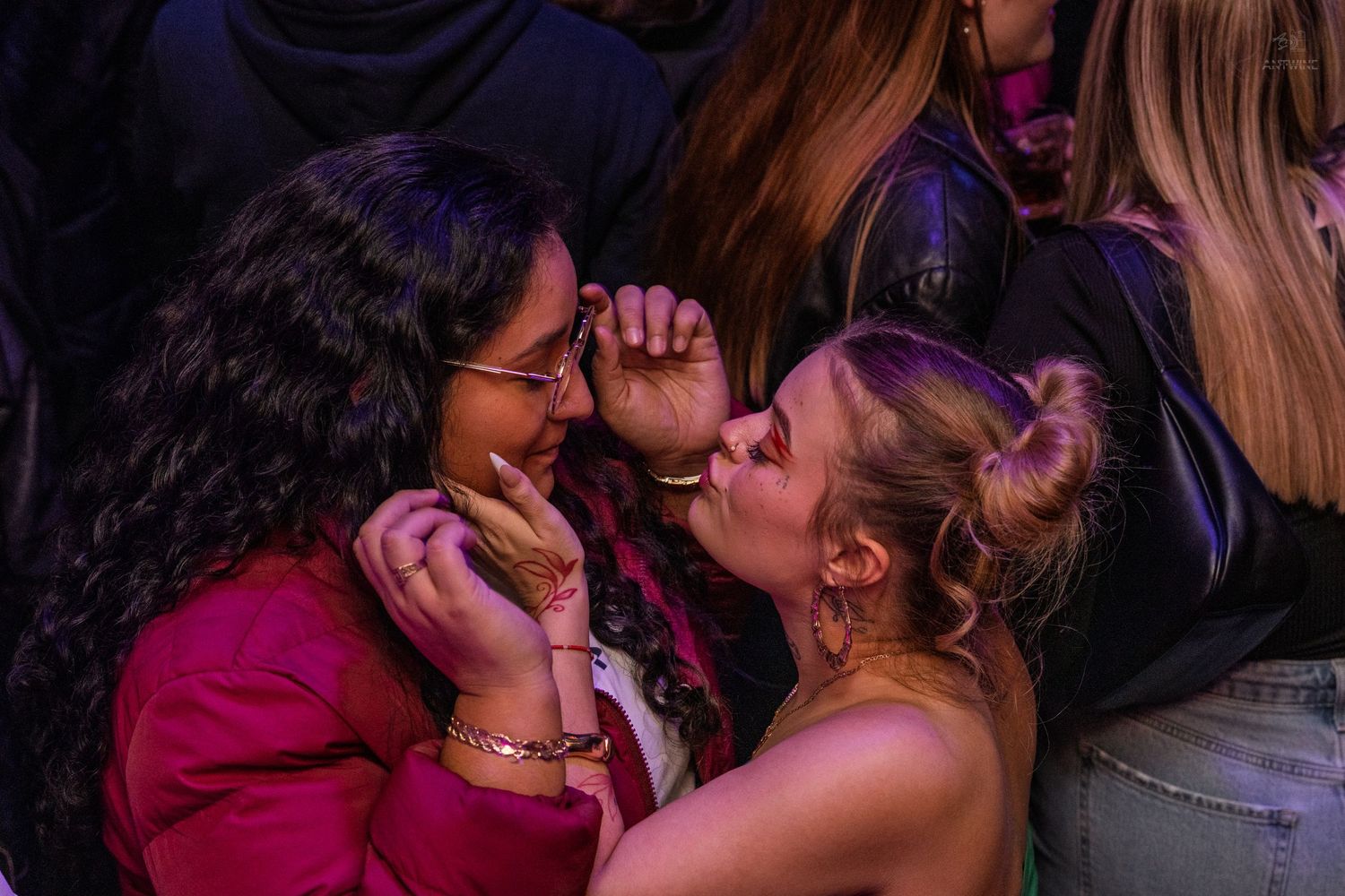 Two young women sharing an intimate moment under blue nightclub lighting.