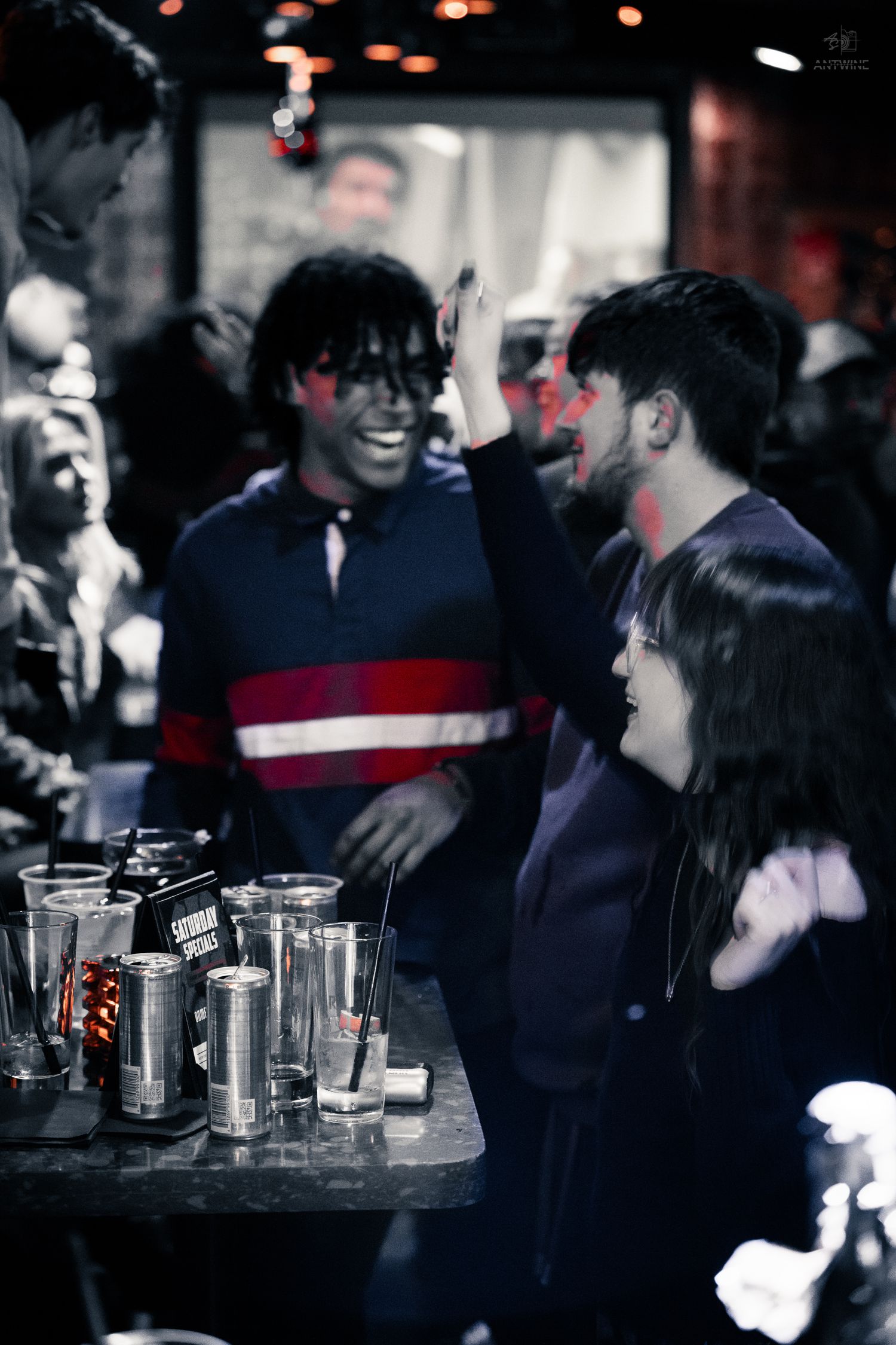 Friends laughing and high-fiving at a bar counter in a black and white edited party photo.