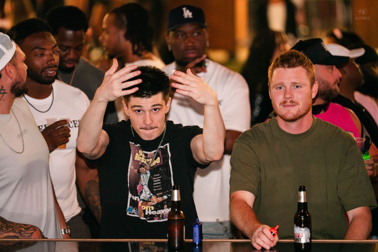 Young man with hands raised expressively at a crowded bar or sports watching event.