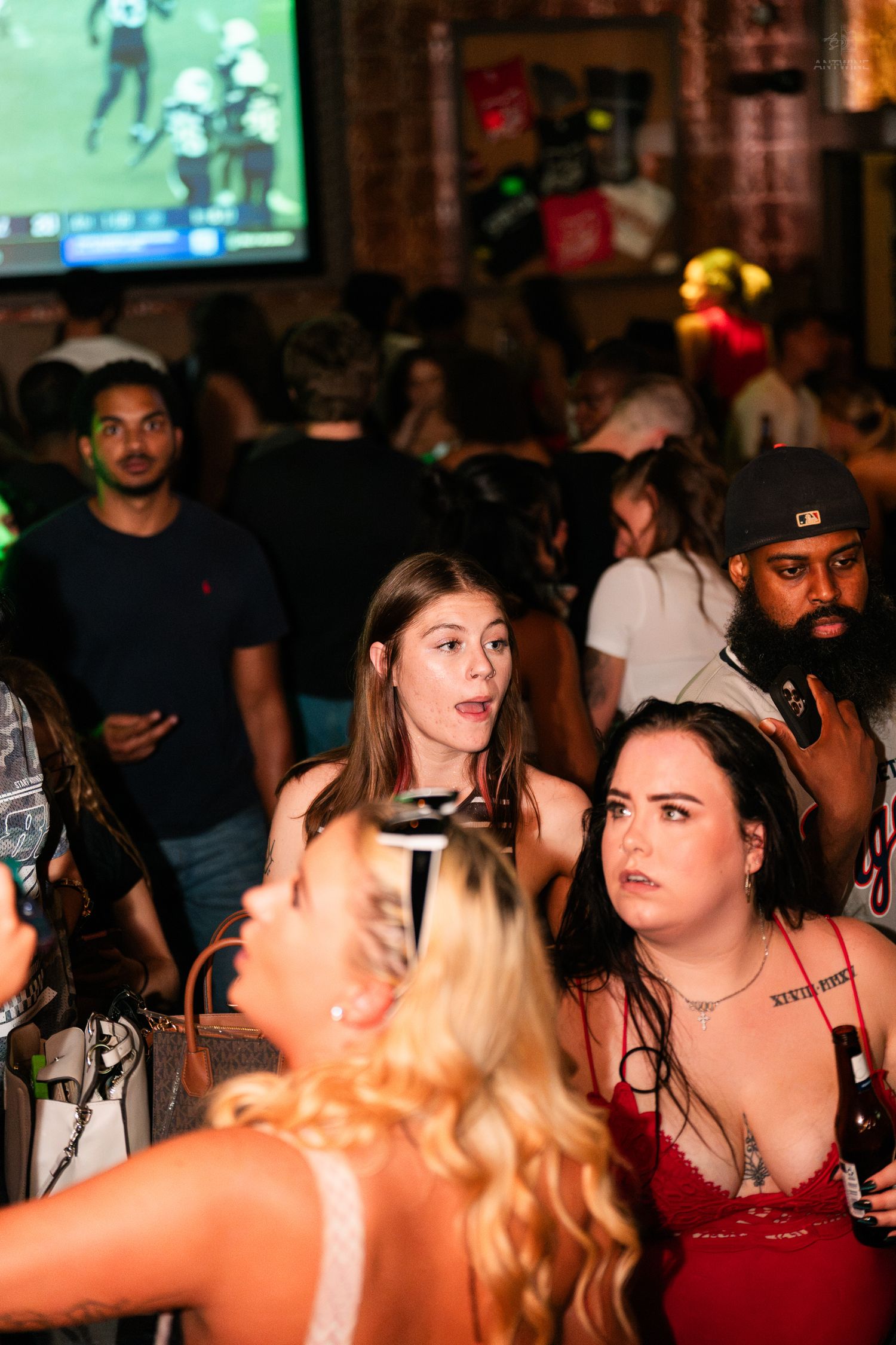Group of friends watching football on big screen TV at a crowded sports bar.