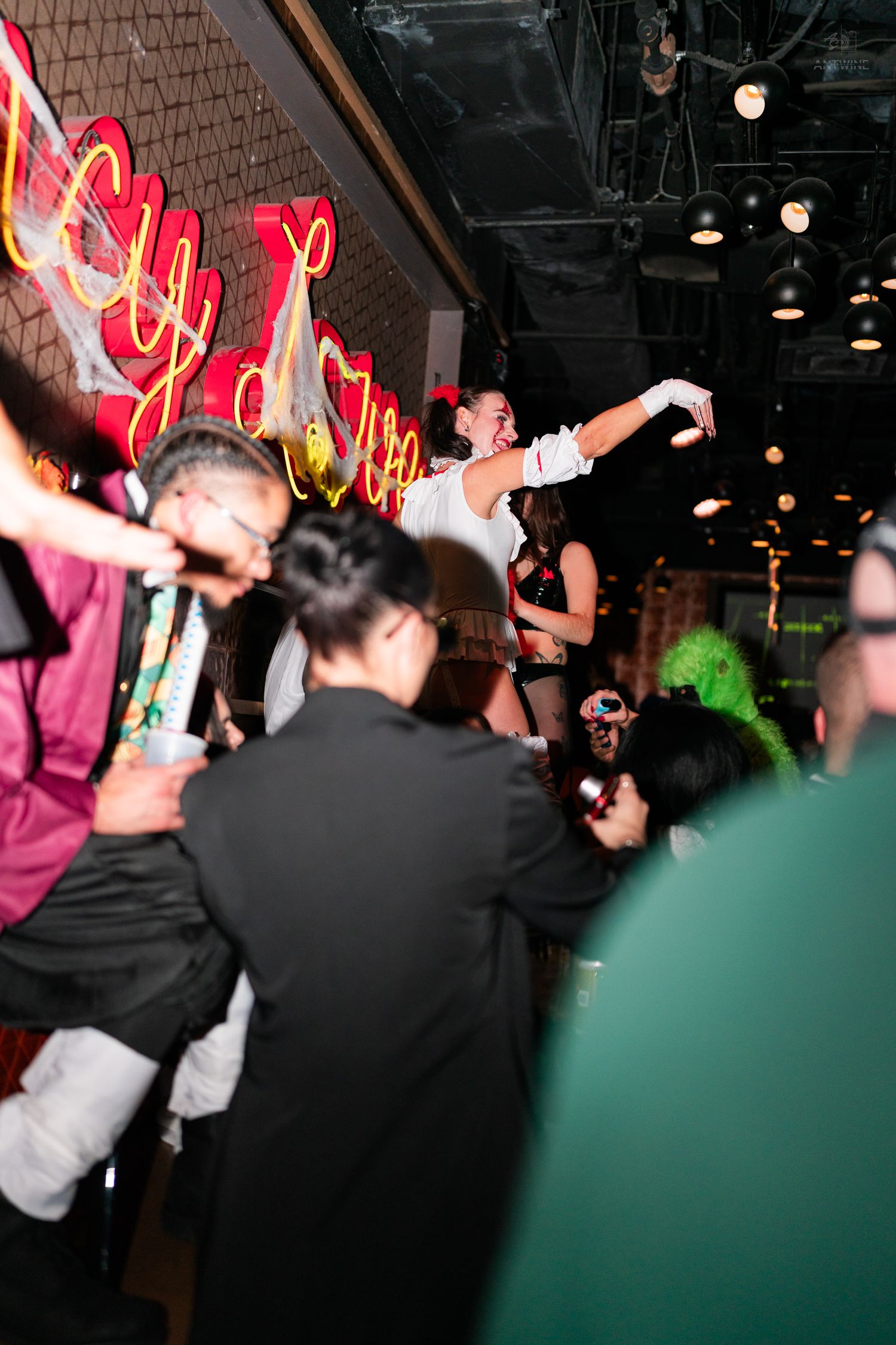 Performer in white costume dancing on a bar at a lively Halloween nightclub event.