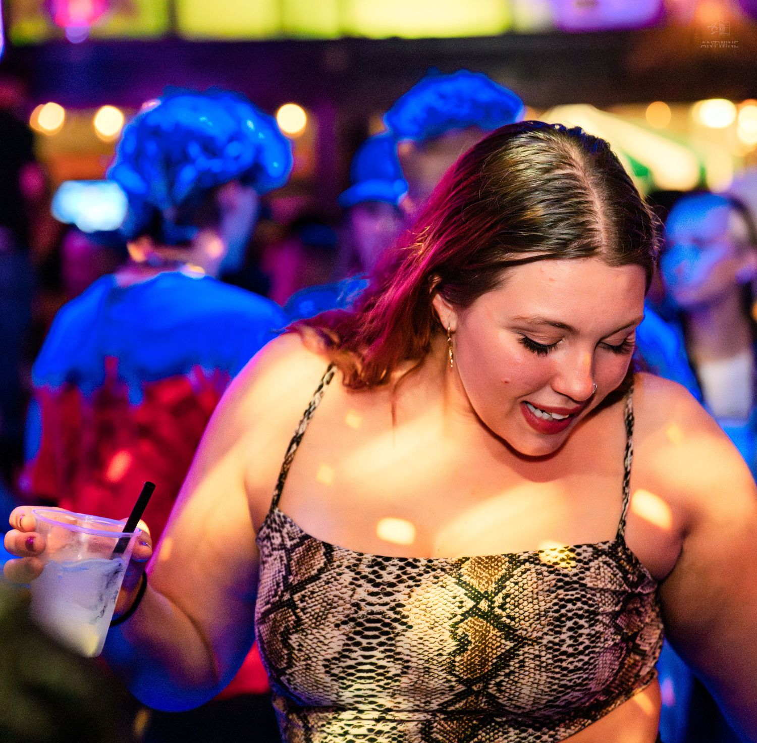 Woman in snakeskin dress laughing and holding a drink at a vibrant nightclub.