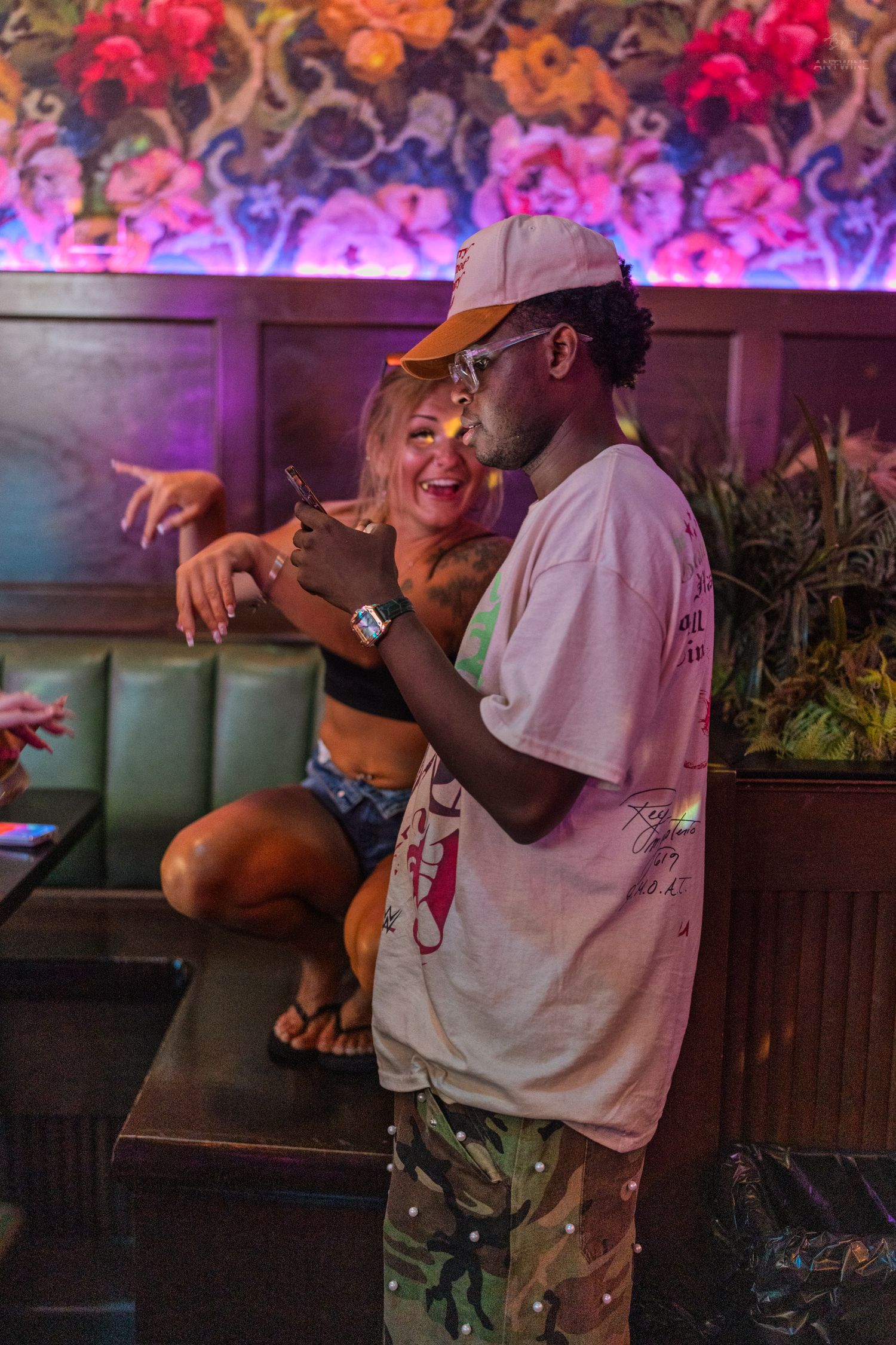 Couple laughing together in a neon-lit nightclub booth with floral decor.