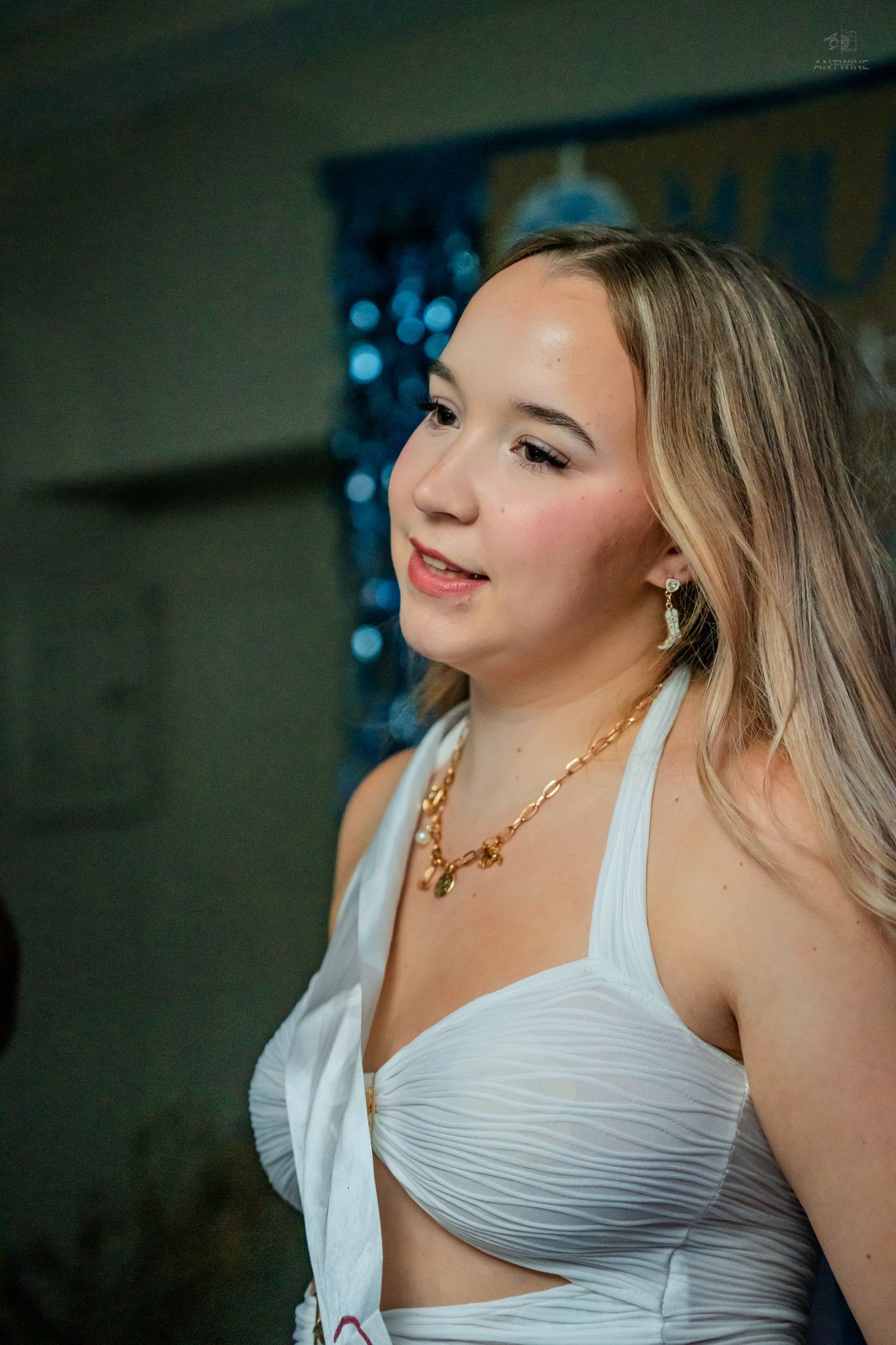 Young blonde woman in white halter top wearing gold chain necklace at a birthday party.