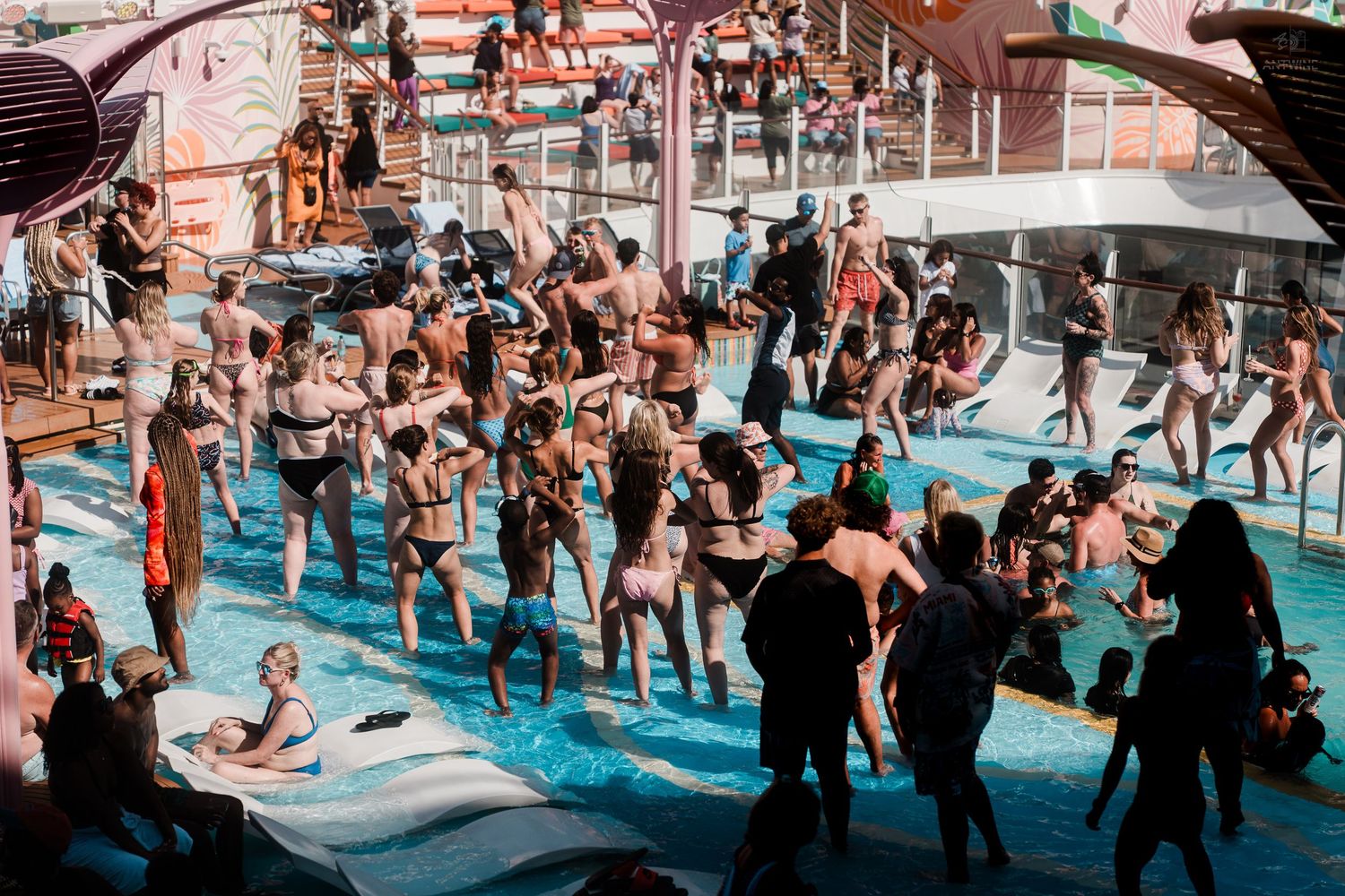 Large crowd of passengers dancing and swimming at a cruise ship pool party.