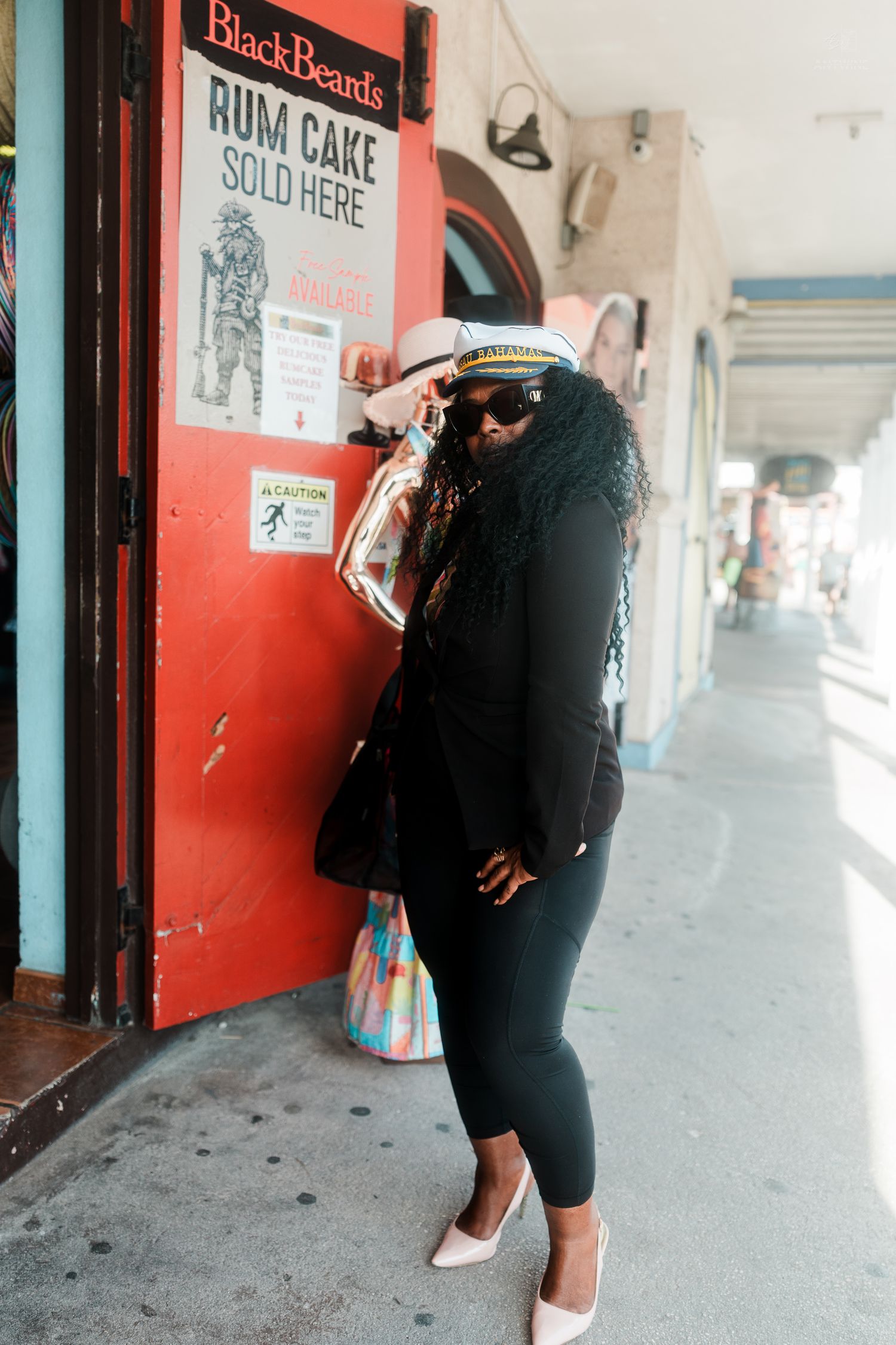 Woman in captain hat posing outside BlackBeards Rum Cake shop on a Caribbean street.