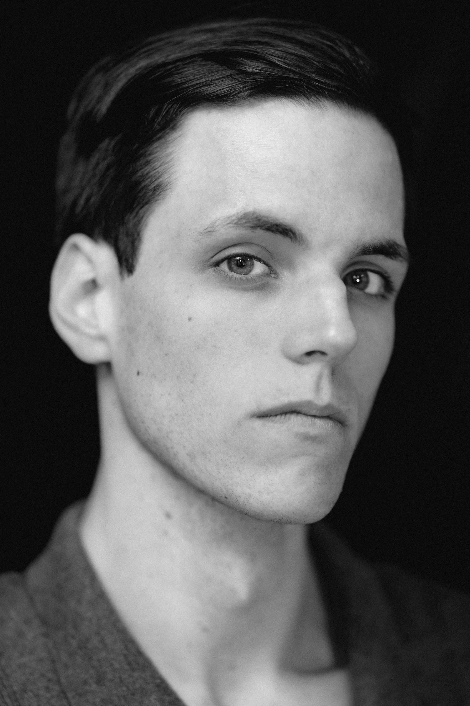 Black and white close-up portrait of a young man with short dark hair and defined facial features.