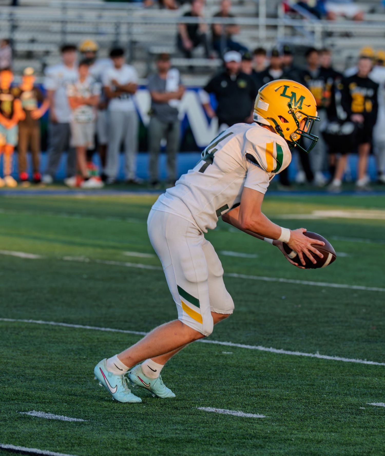 A football player in white LM uniform fields the ball on the green turf during a high school football game.
