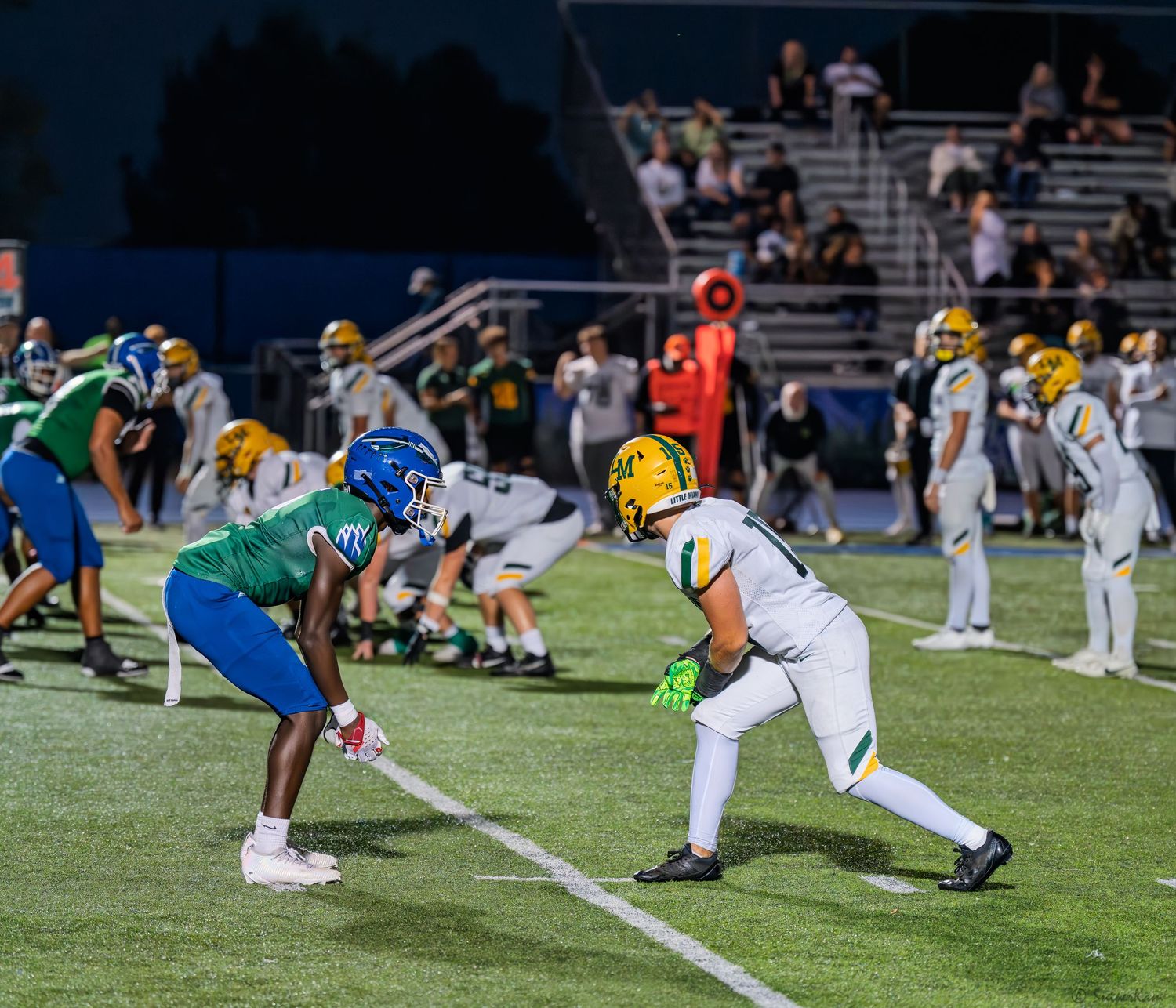 Two high school football players face off at line of scrimmage during evening game.