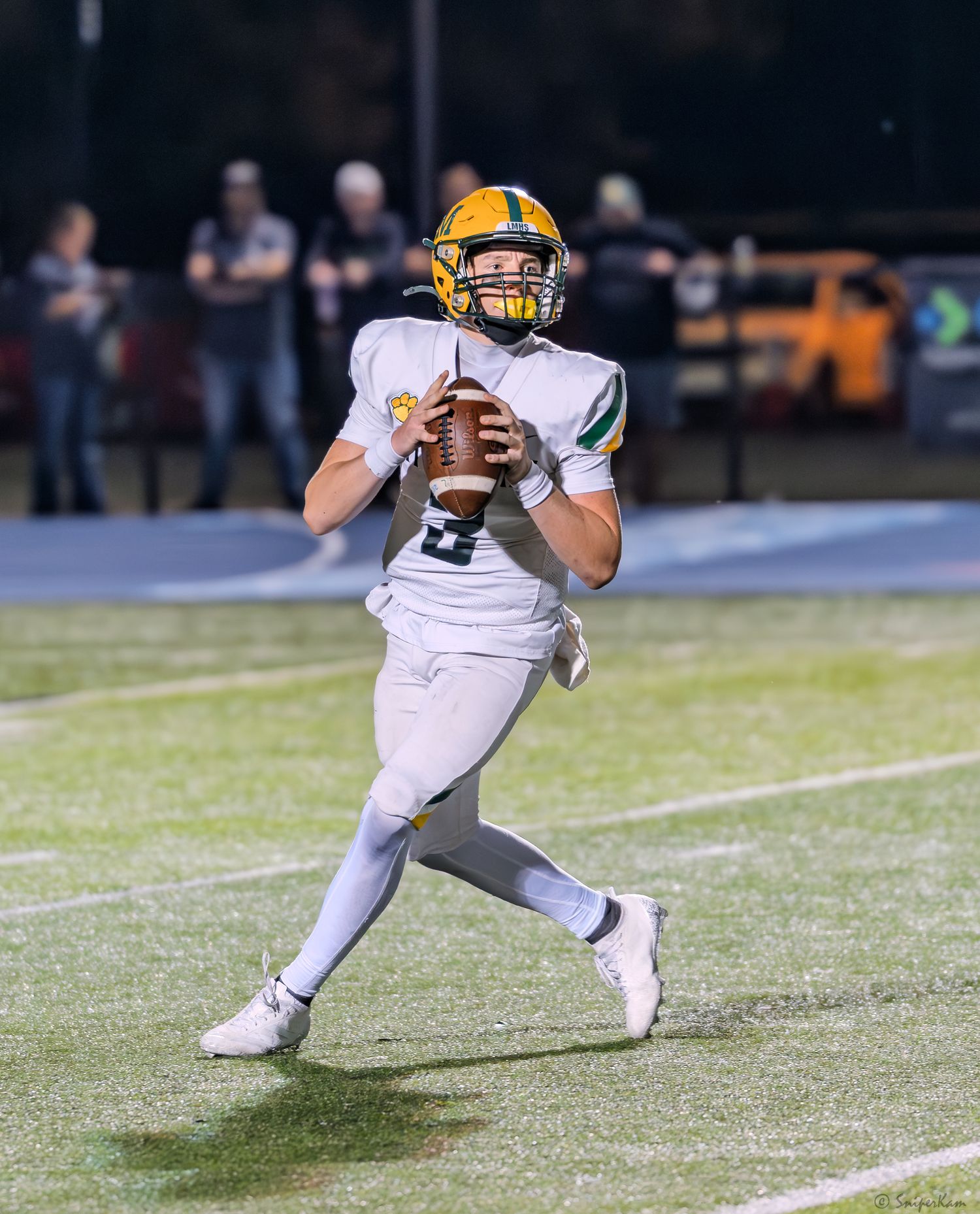 High school quarterback #3 in white uniform drops back to pass during a night football game.