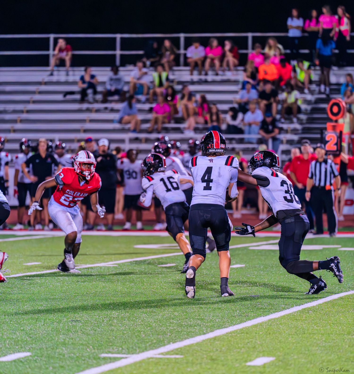 High school football player in red uniform runs the ball against black and white uniformed defenders.