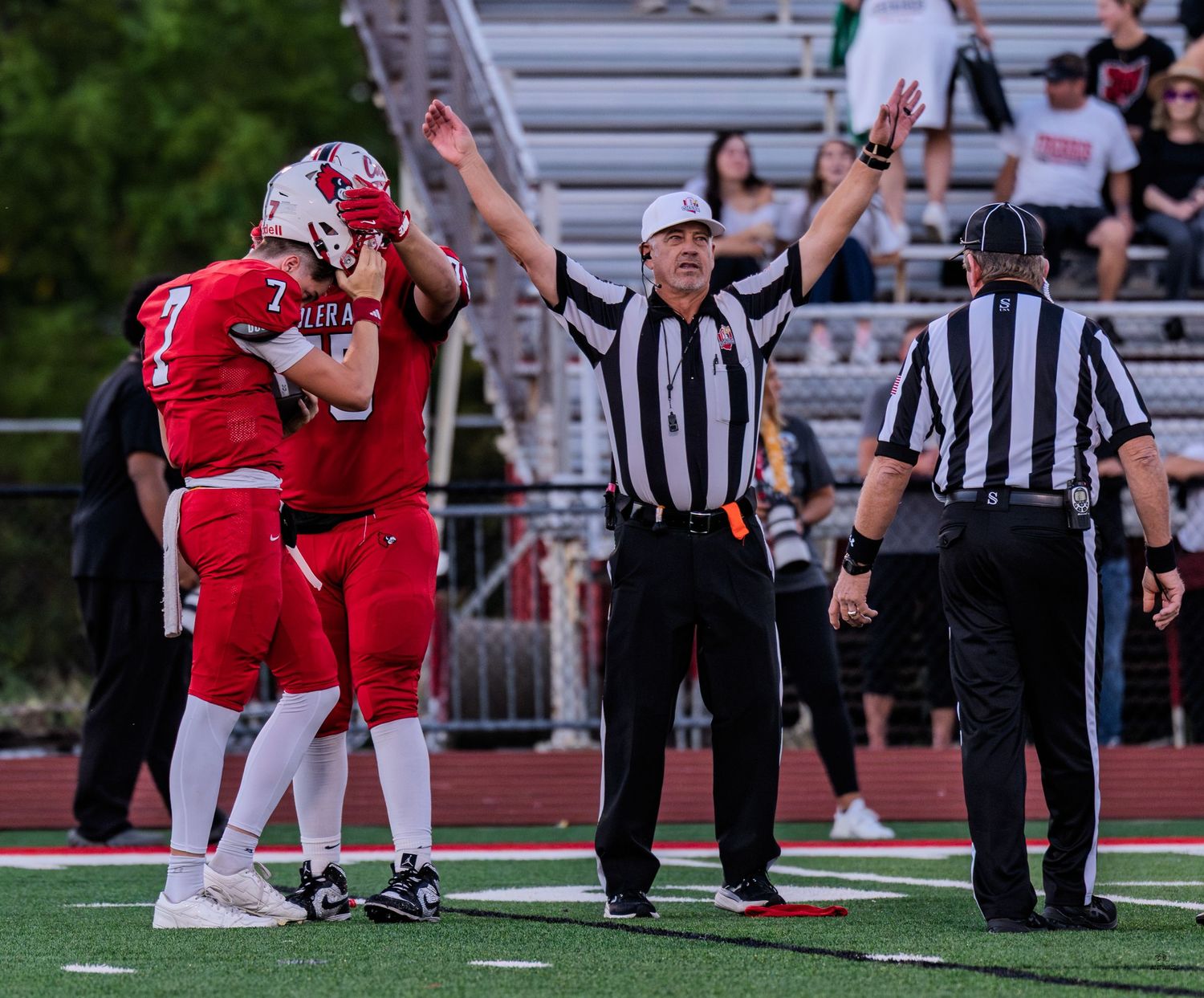 Referee signals touchdown as two red-uniformed football players embrace during a high school football game.