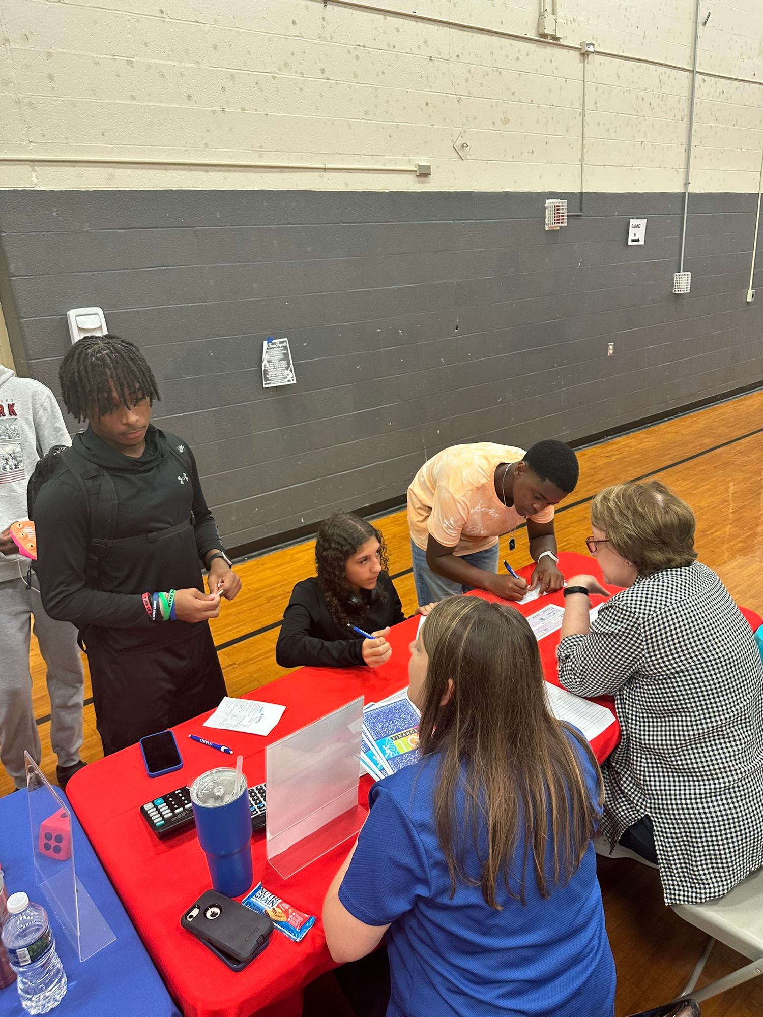 Students gather around a red table with advisors during a school career fair event in a gymnasium.