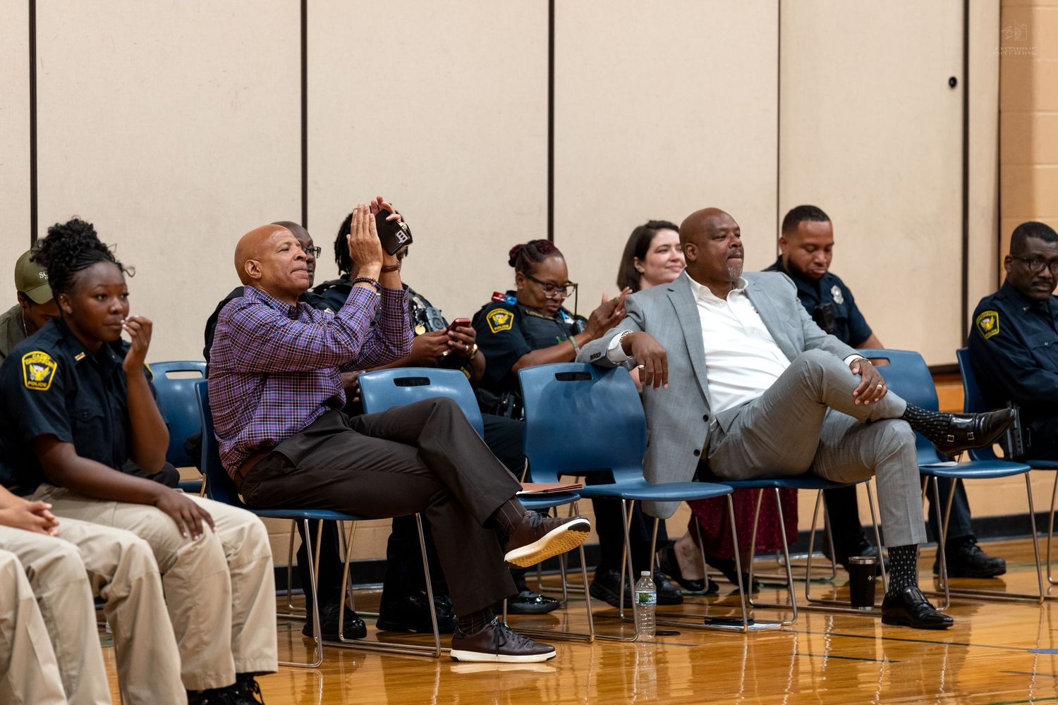 Diverse group of adults seated in chairs at an indoor community event in a gymnasium setting.