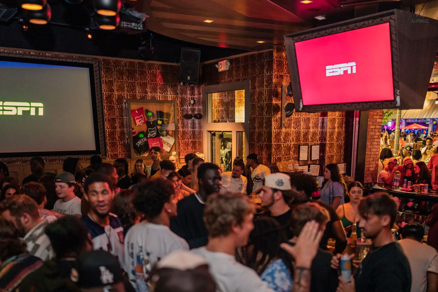Energetic crowd fills a sports bar watching ESPN broadcast on large projection screens.