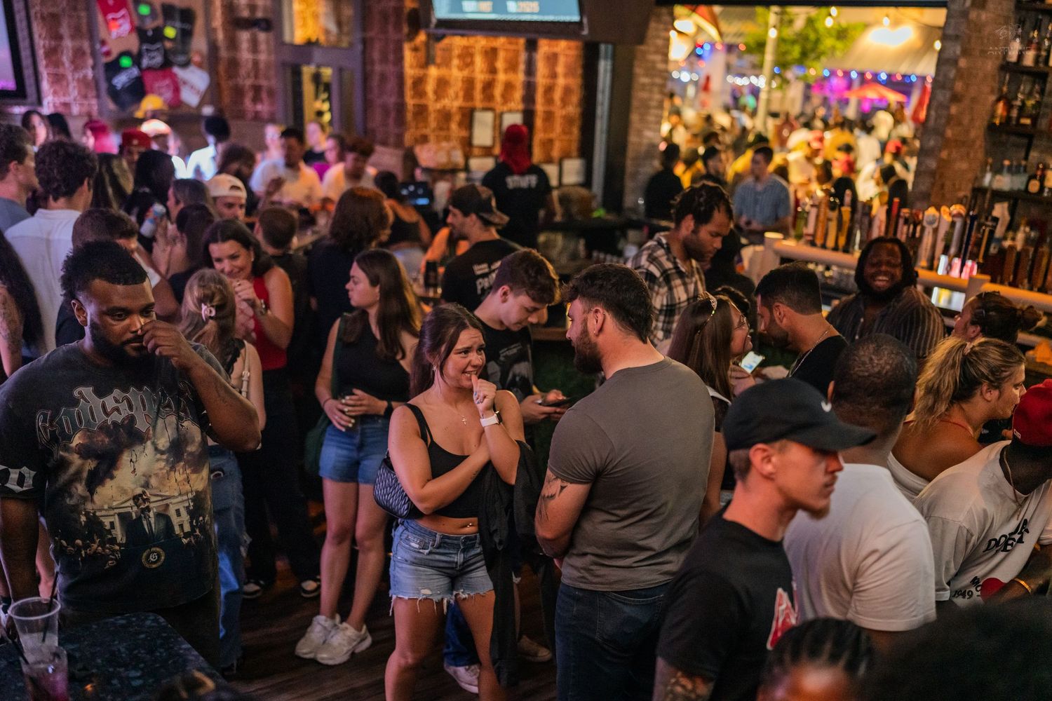 Large crowd of young adults socializing and dancing at a packed bar.