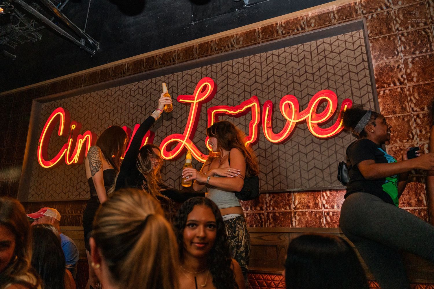 Crowd dancing and celebrating under the Cincinnati Love neon sign at a bar.
