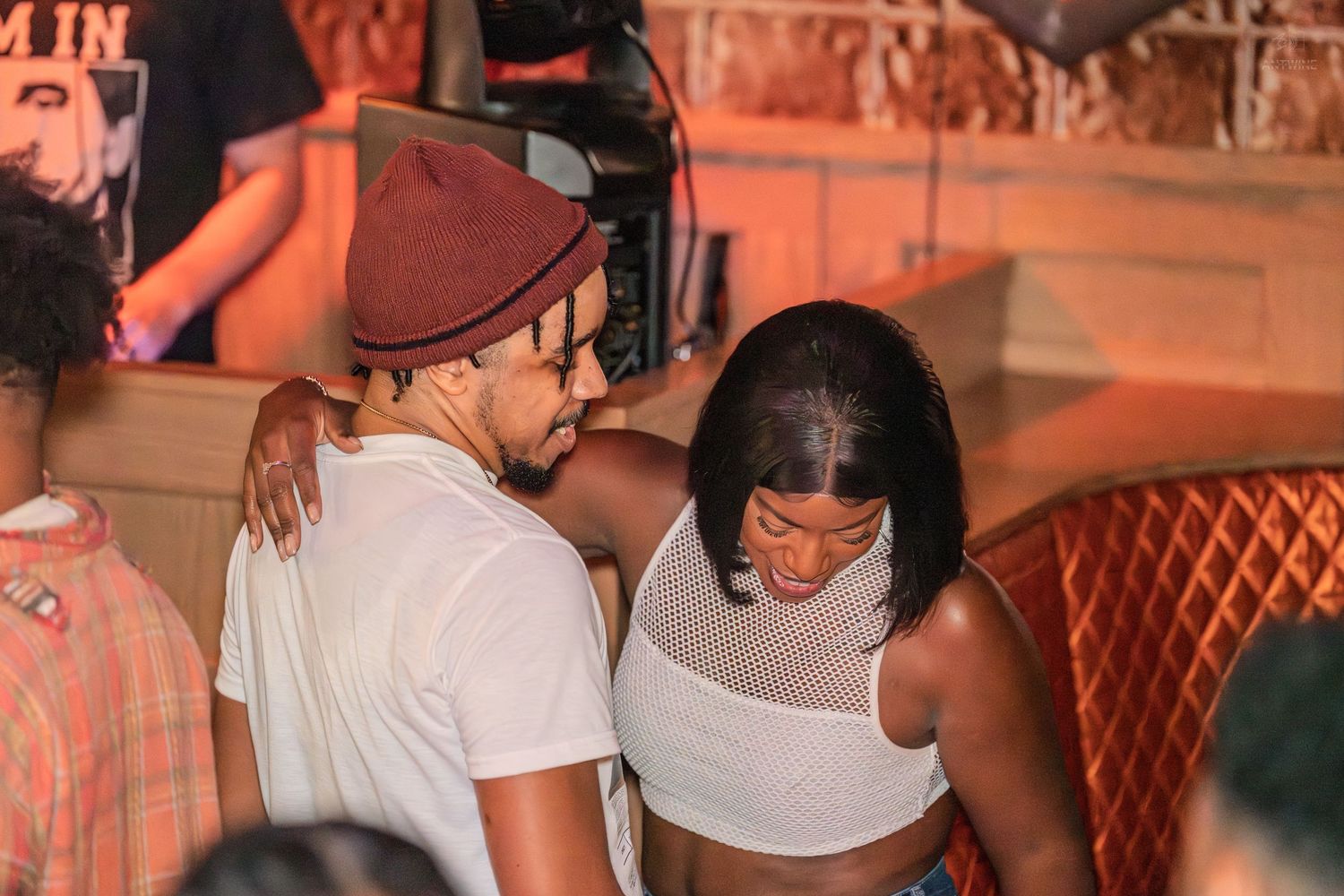 Young couple dancing closely together in a vibrant nightclub with DJ in background.