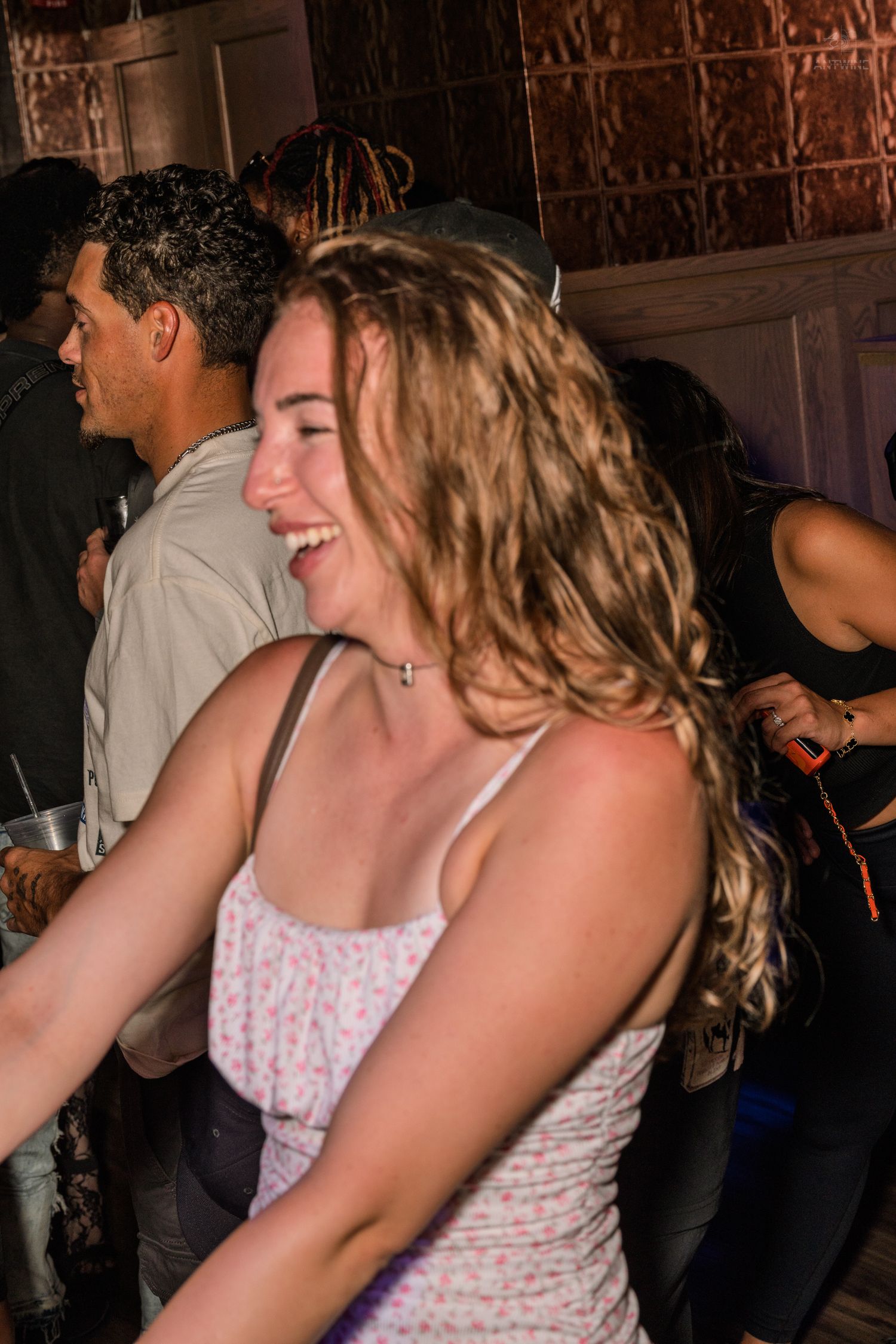 Young woman with curly hair laughing joyfully at a crowded nightclub party.
