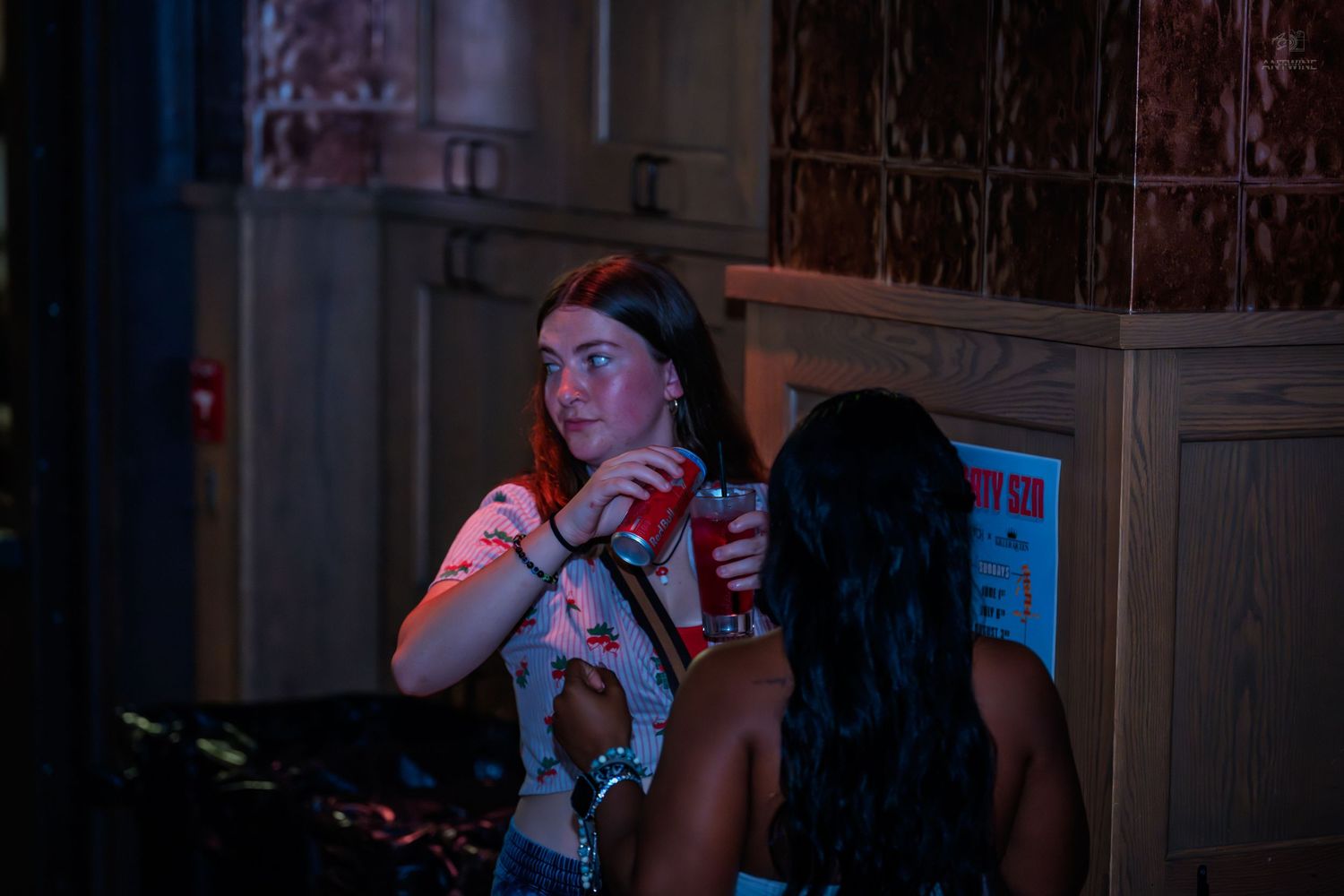 Two young women chatting at a nightclub, one holding a red cup.