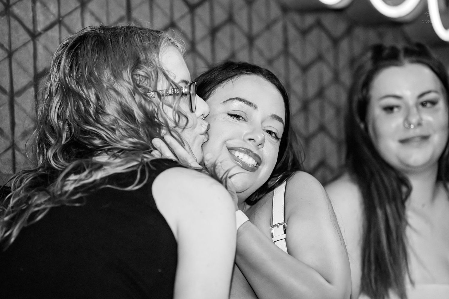 Two women sharing a joyful hug while smiling at a nightclub with neon decor.