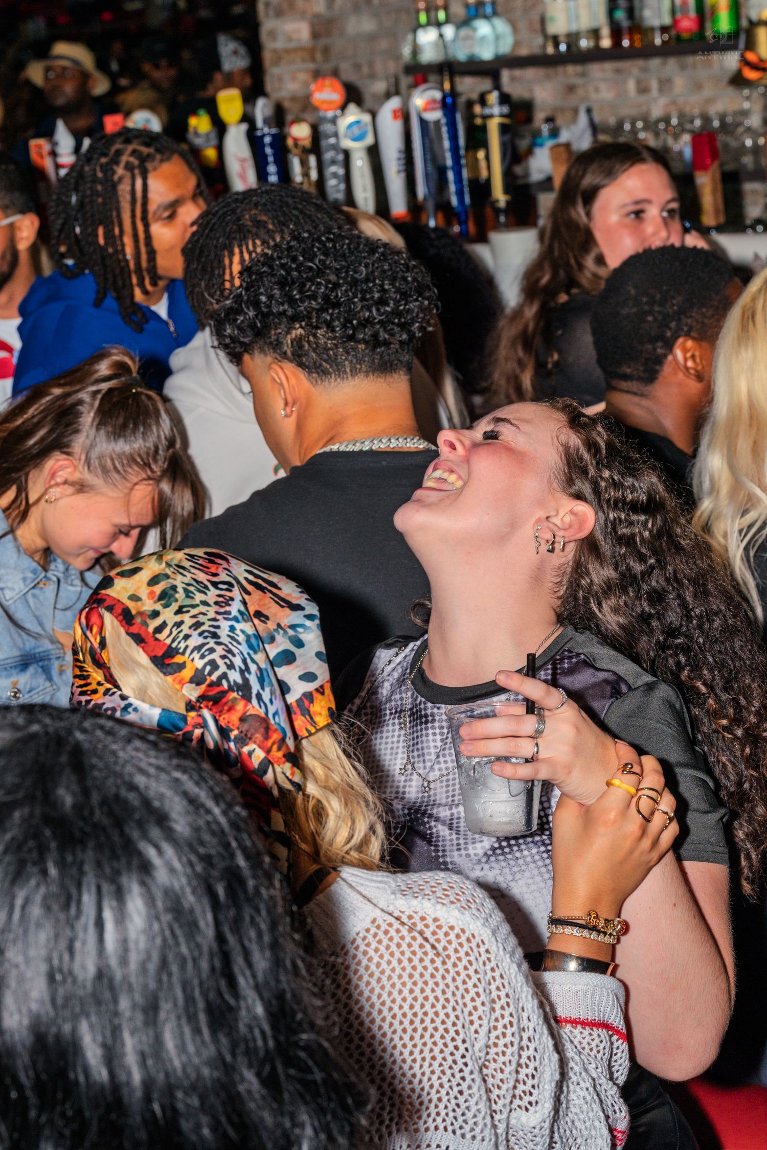 Woman laughing joyfully while socializing in a crowded bar with friends nearby.