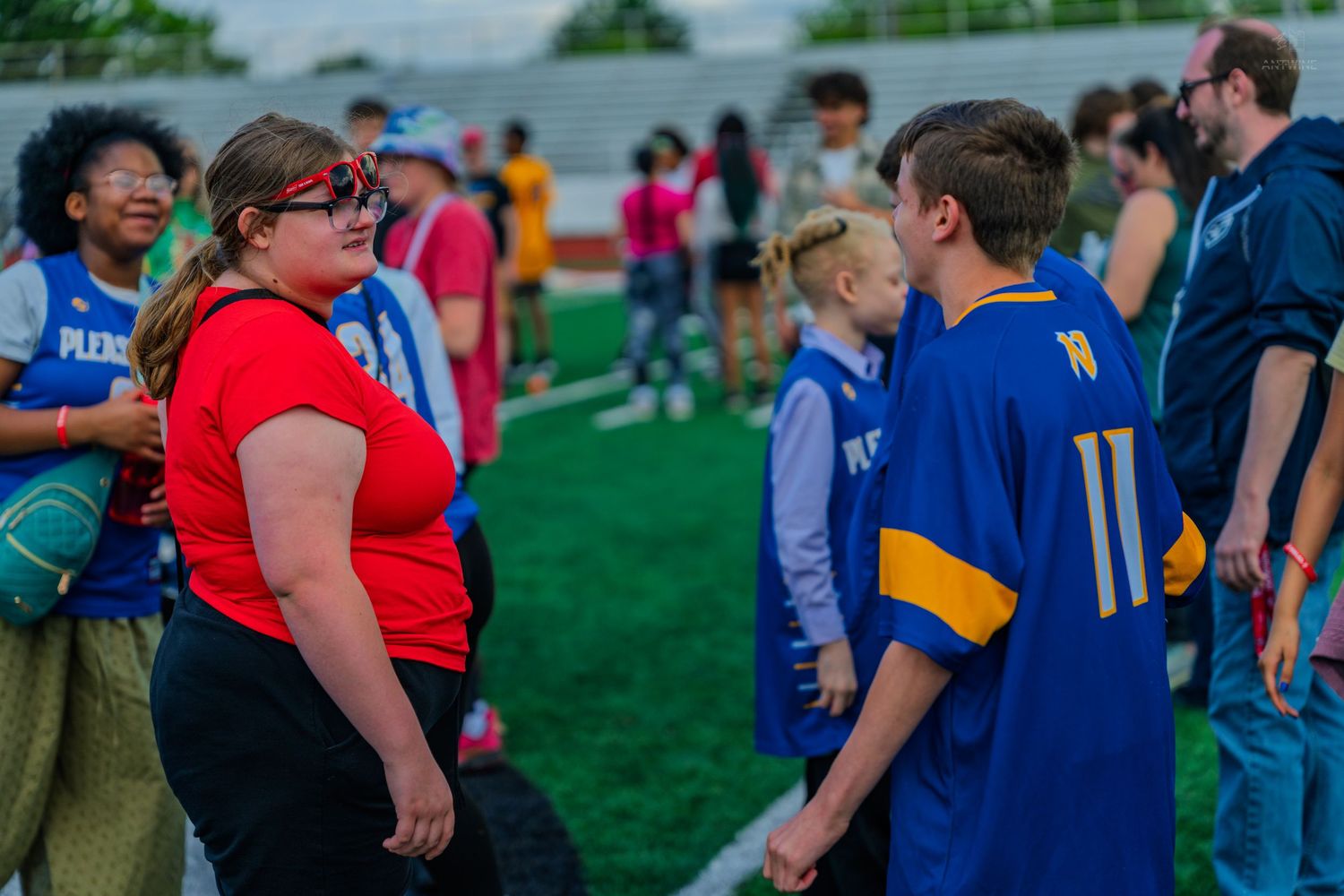 Students in sports jerseys gather on a green turf field during an outdoor school athletic event.