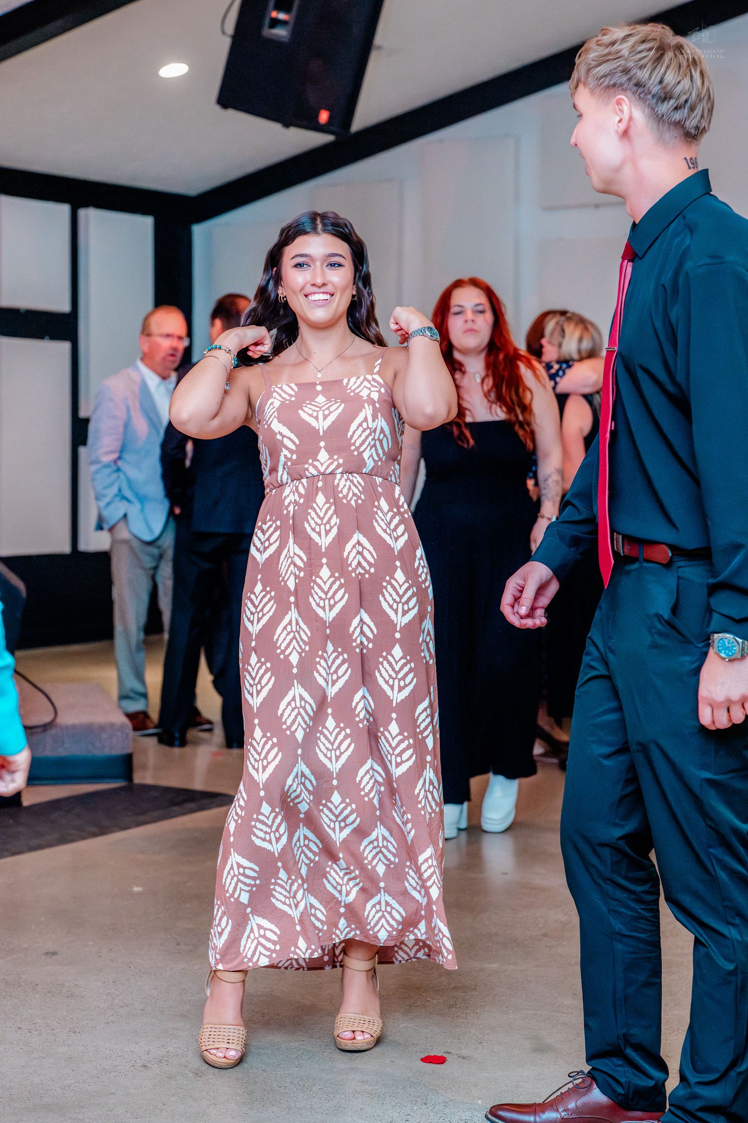 Young woman in floral maxi dress smiling at a formal event with guests in background.