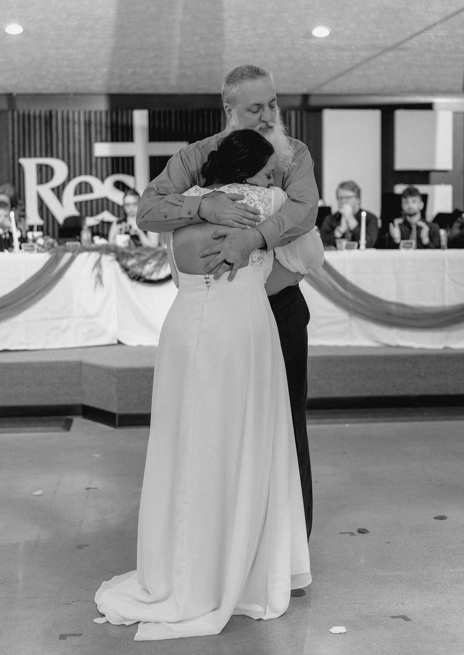 Black and white photo of bride and older man sharing emotional father-daughter dance at wedding reception.