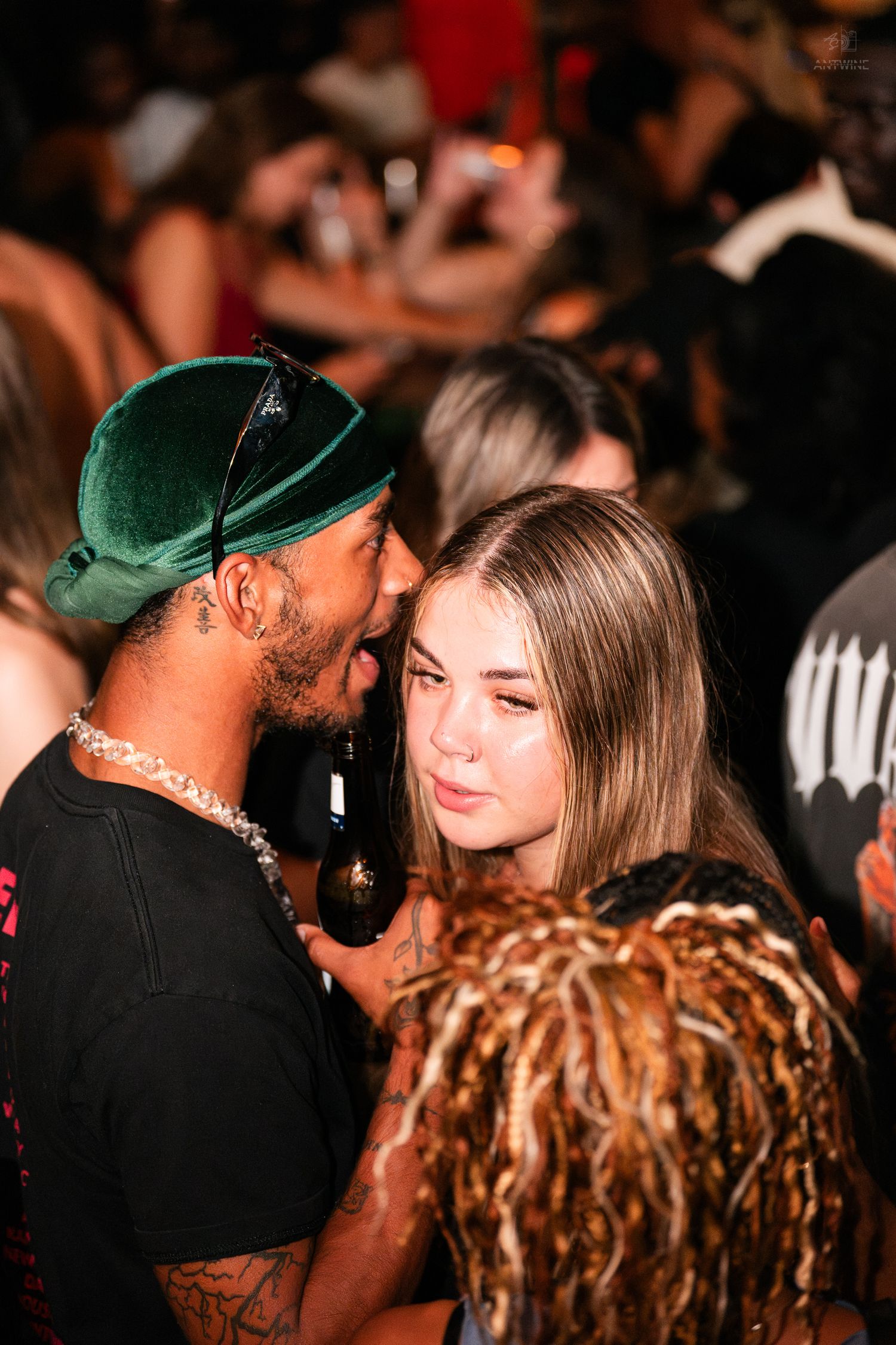 Man in green cap whispering to blonde woman in a crowded nightclub.