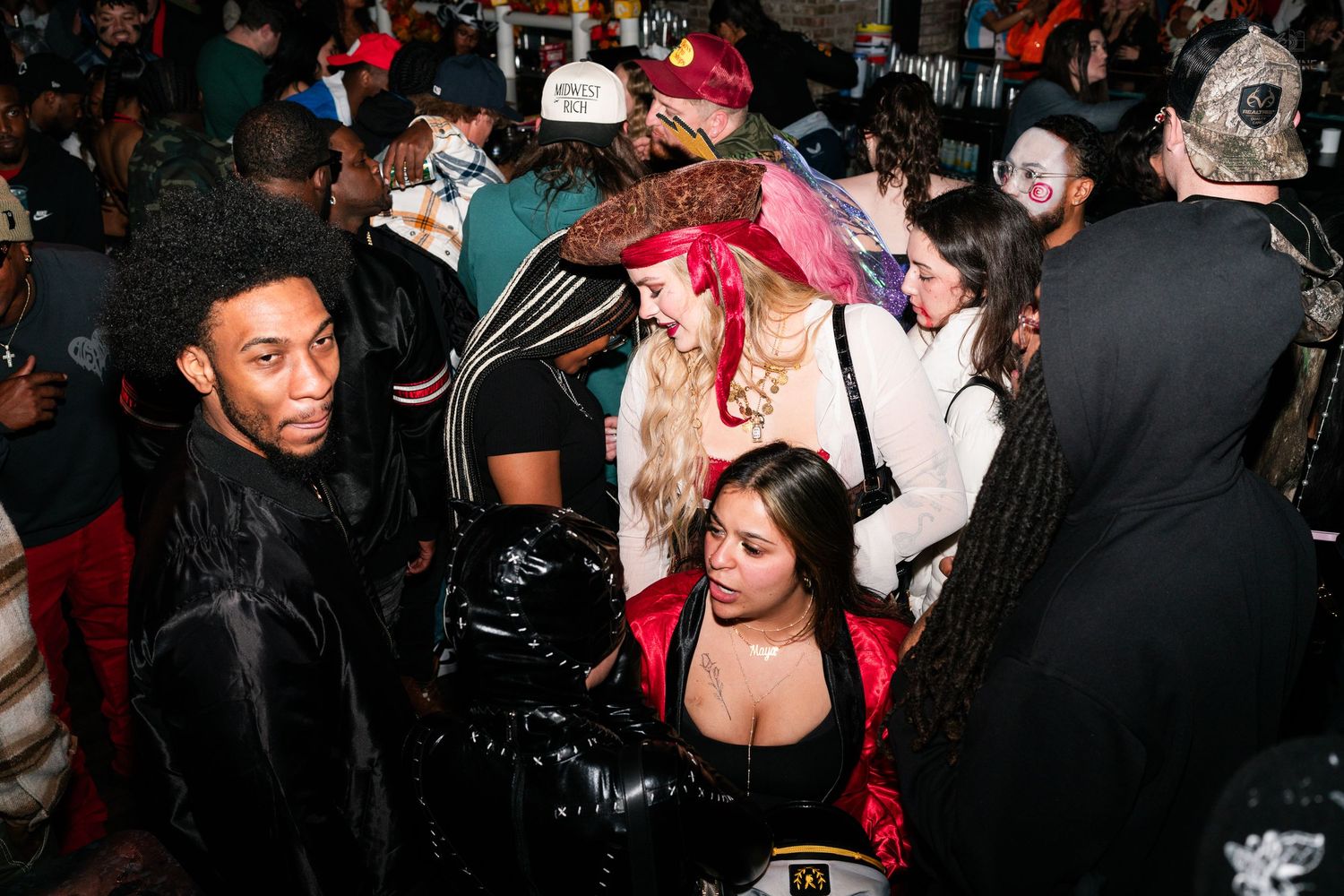 Diverse crowd in Halloween costumes at a lively indoor party event.