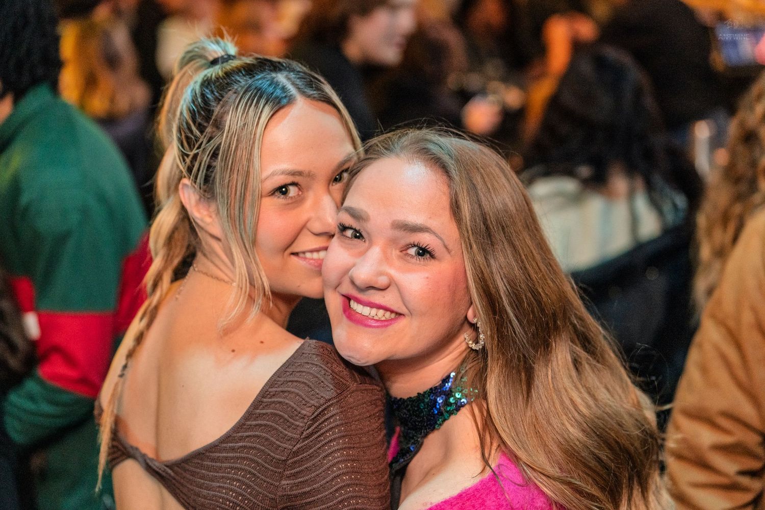 Two smiling women hugging and posing together at a nightclub event.