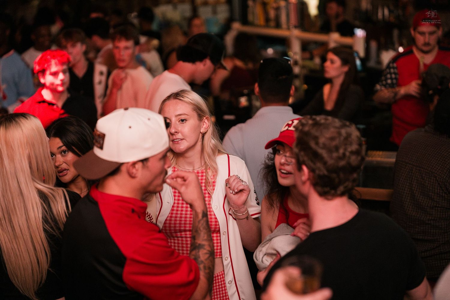 Group of young adults chatting and laughing together at a crowded indoor bar event.