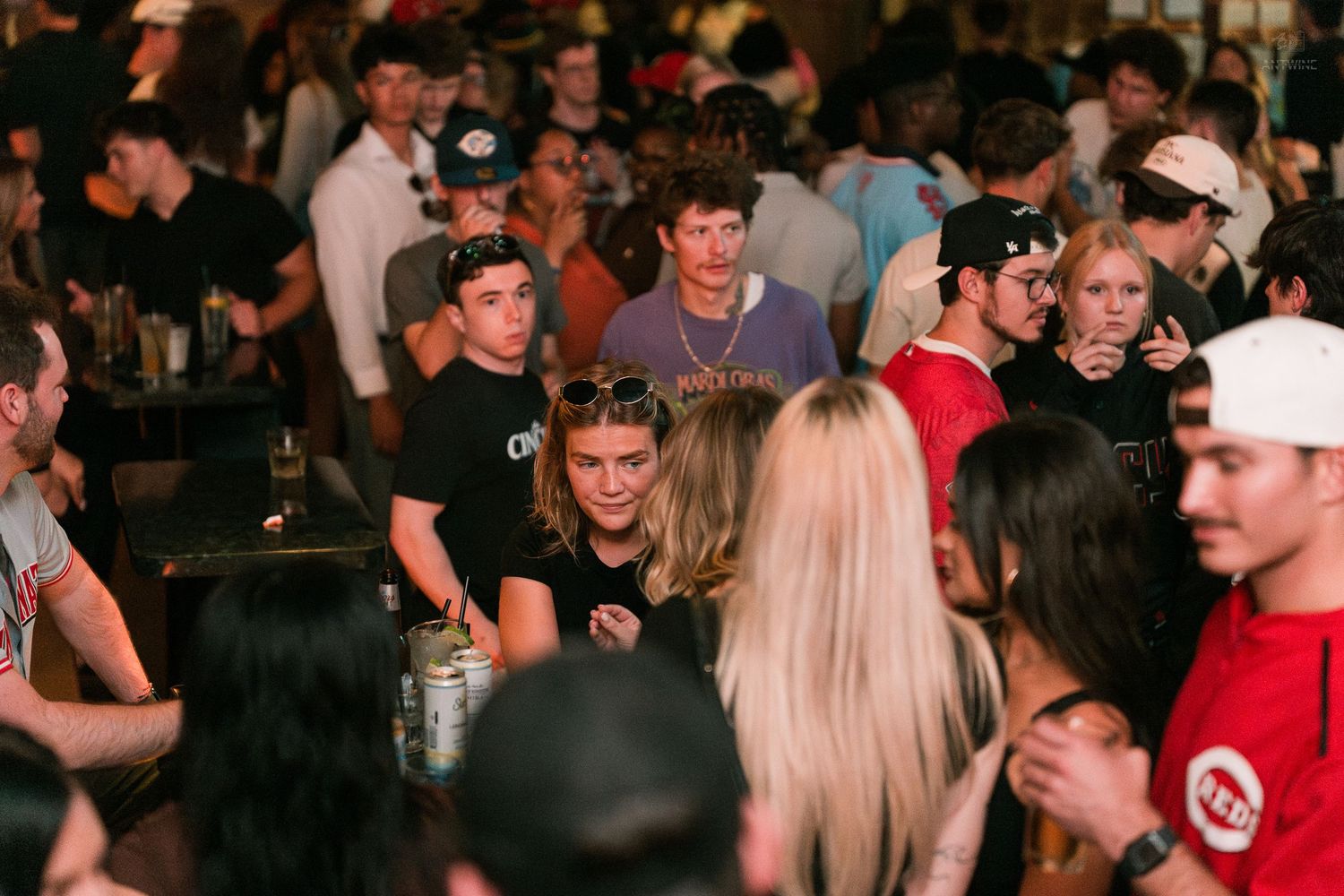 A large crowd of young people socializing and mingling inside a busy bar with warm ambient lighting.