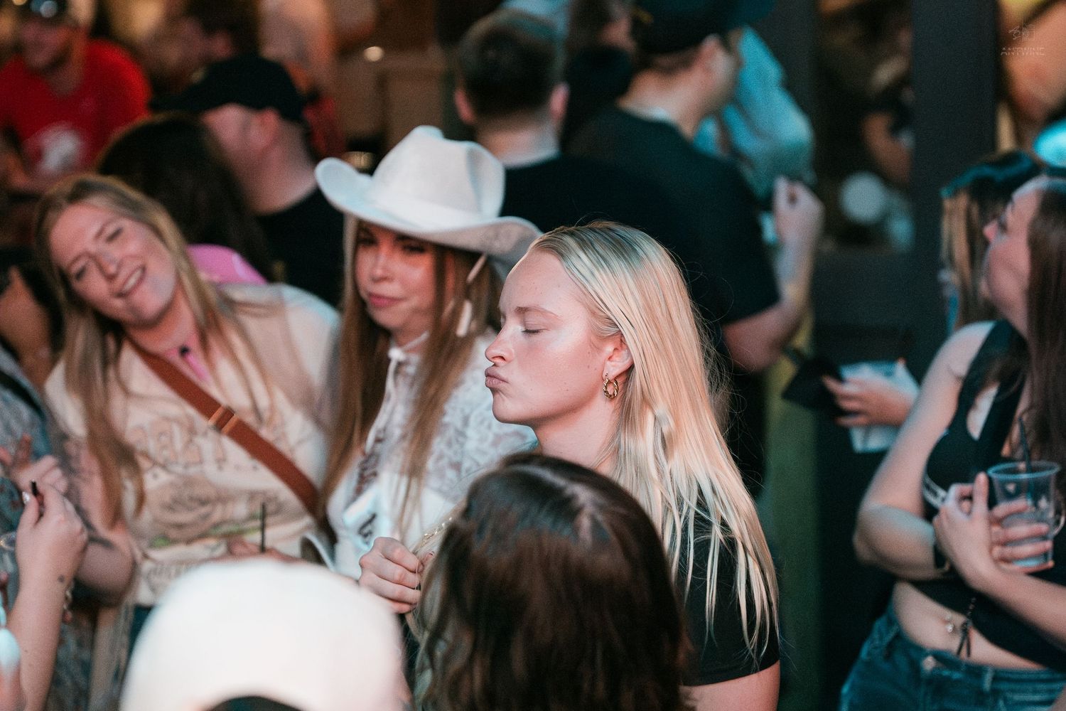 Women in cowboy hats socialize and dance at a lively country-themed bar night event.