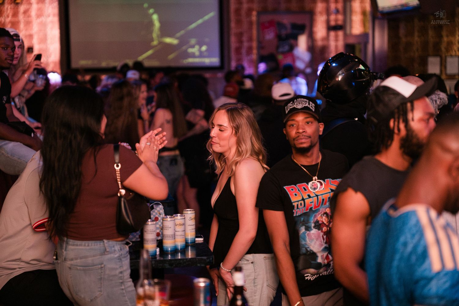 Diverse group of partygoers socialize and dance in a vibrant, crowded nightclub setting.