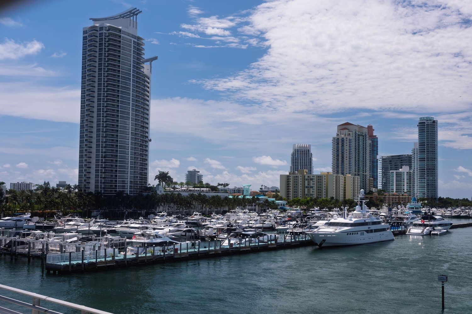 Miami marina with luxury yachts and high-rise buildings under a partly cloudy blue sky.