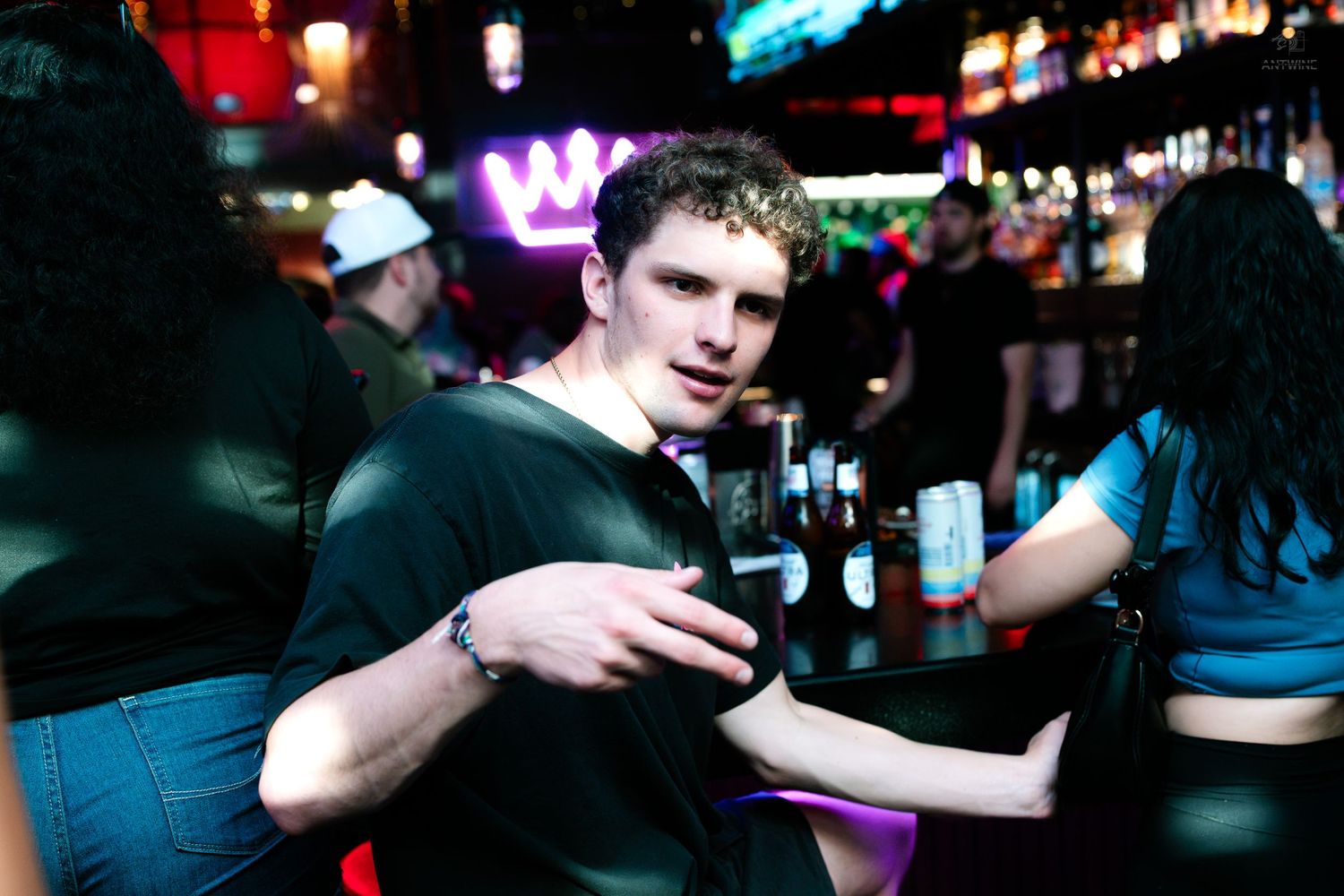 Young man holding a beer bottle smiling at a lively neon-lit nightclub.