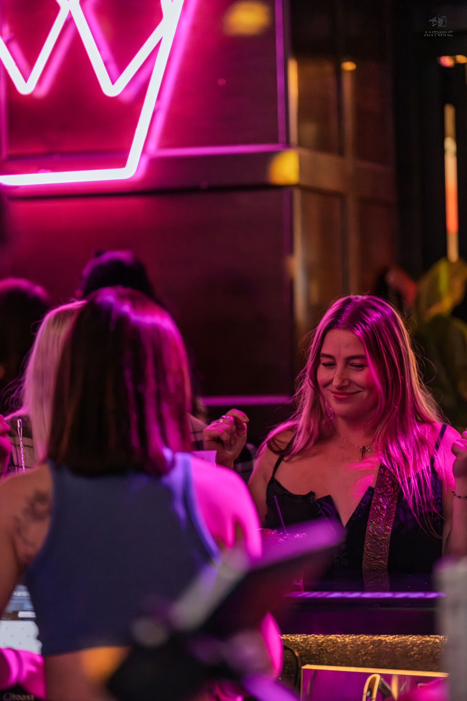 Woman smiling warmly while socializing at a bar illuminated by pink neon lights.