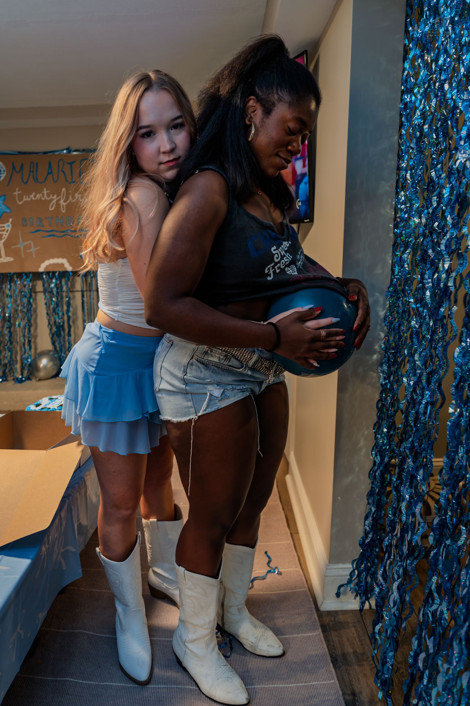 Two young women posing together at a blue-themed birthday party celebration.