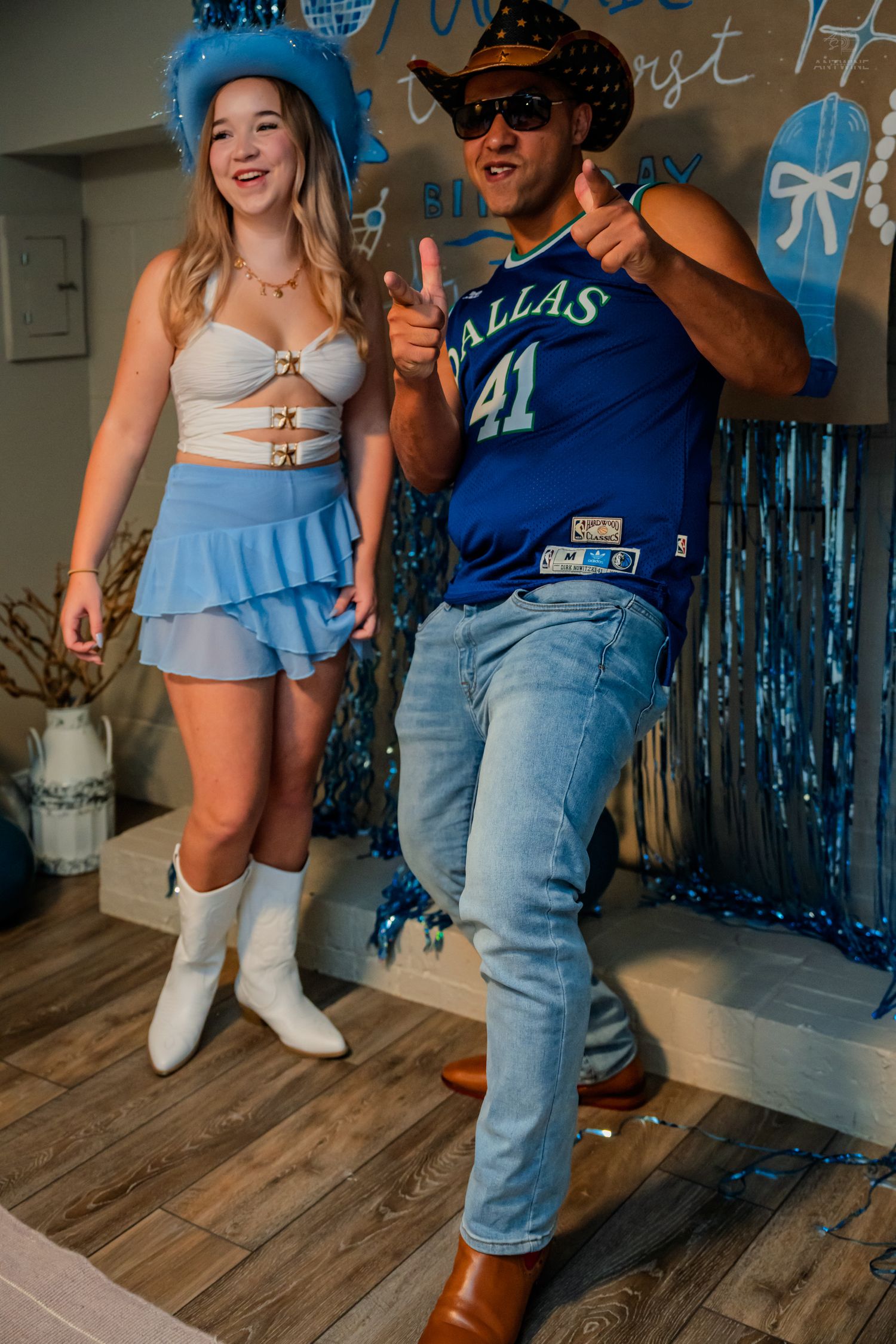 Smiling couple in blue Western and sports outfits celebrate at a blue-themed birthday party.