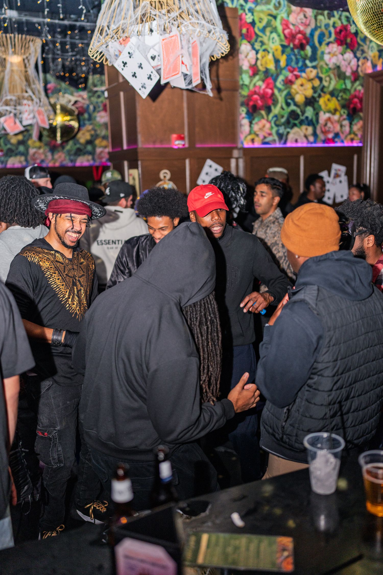 Group of friends socializing and shaking hands inside a crowded nightclub with floral wall decor.