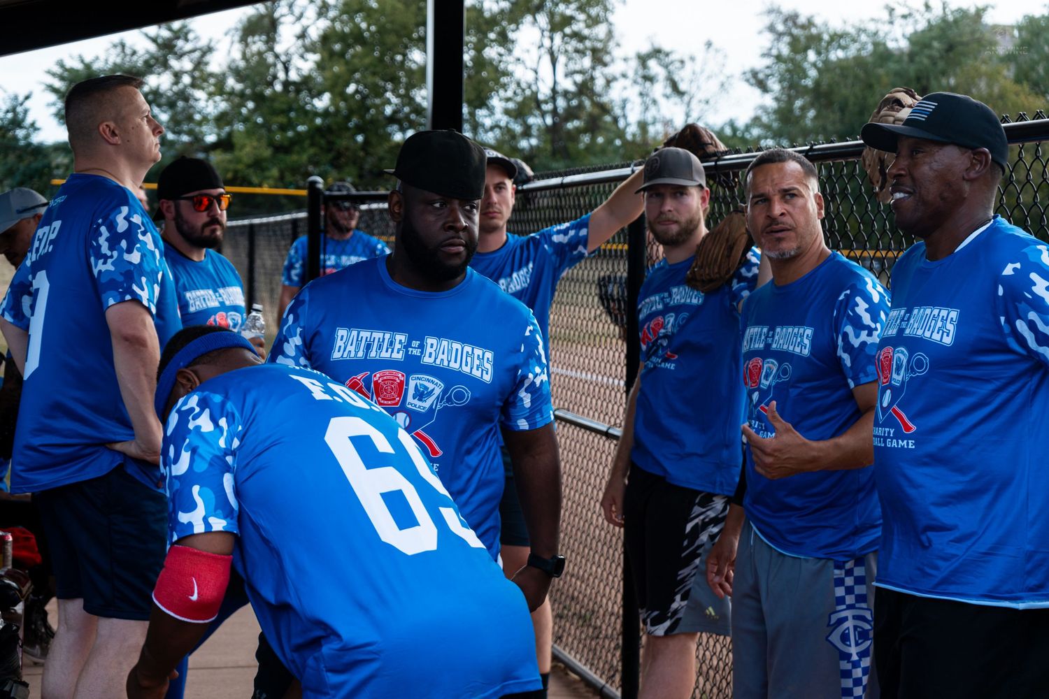 Athletes in blue Battle of Badges uniforms huddle together in dugout during softball event.