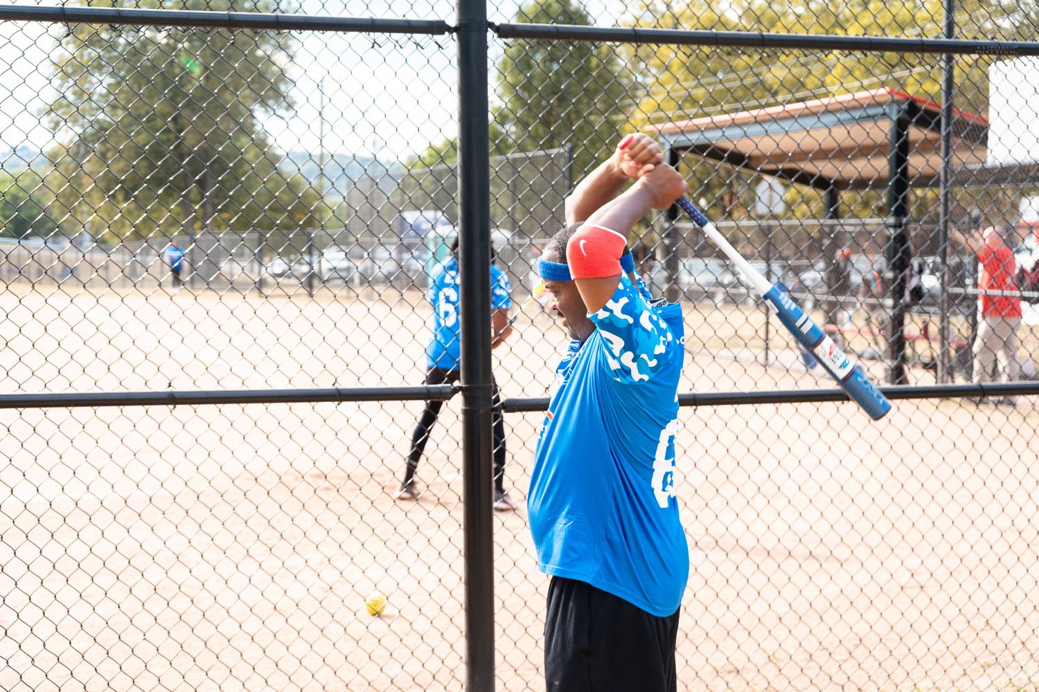 A softball player in blue jersey swings a bat during a charity softball game.