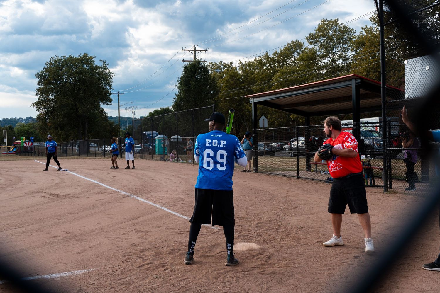 Player wearing jersey number 69 stands at bat during an outdoor softball game on a dirt field with spectators nearby.