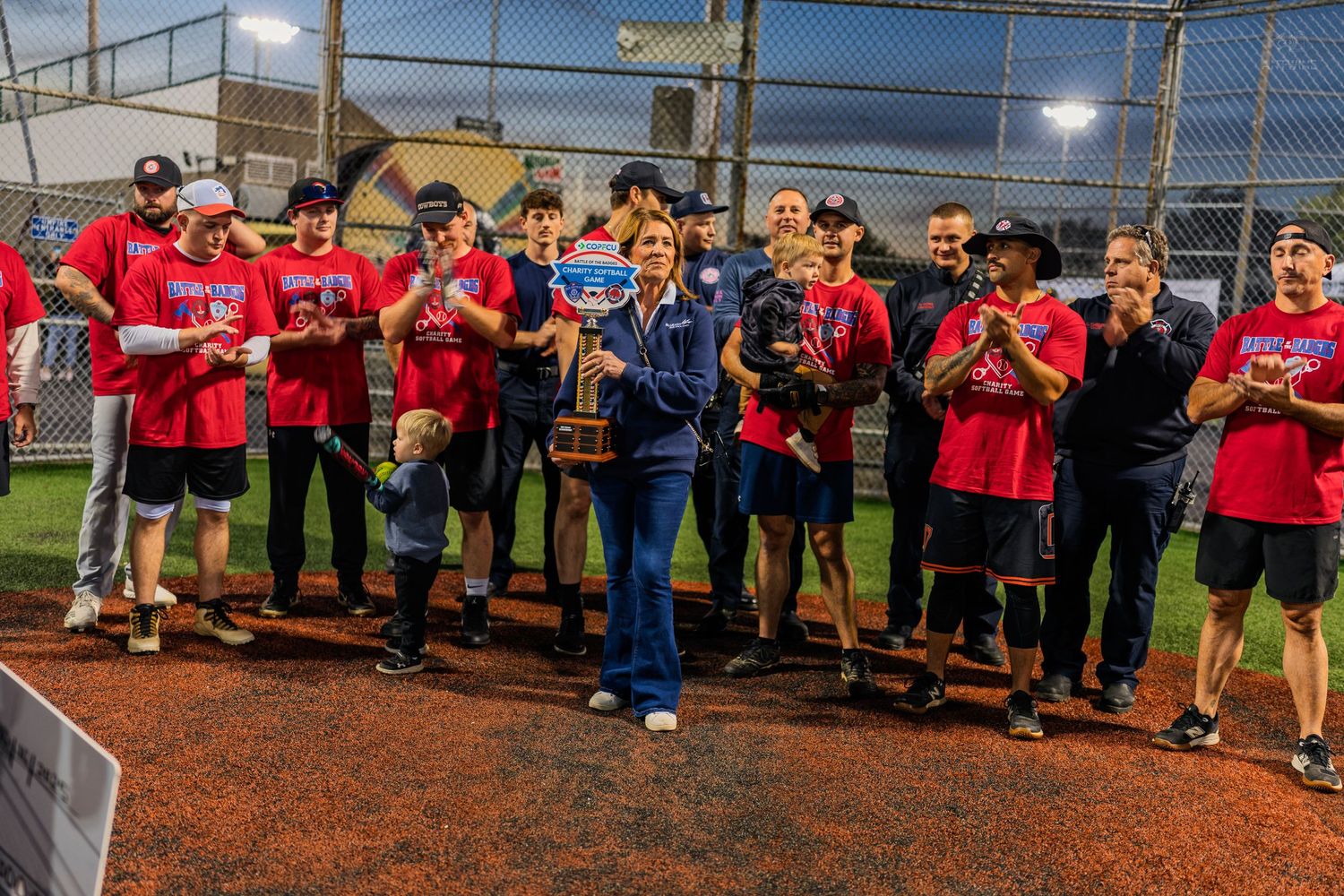 Winning softball team poses with trophy under stadium lights during nighttime awards ceremony.